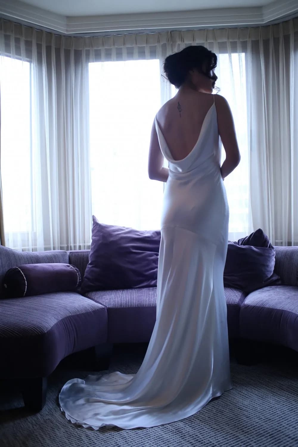 Bride viewed from behind in a draped white gown indoors.