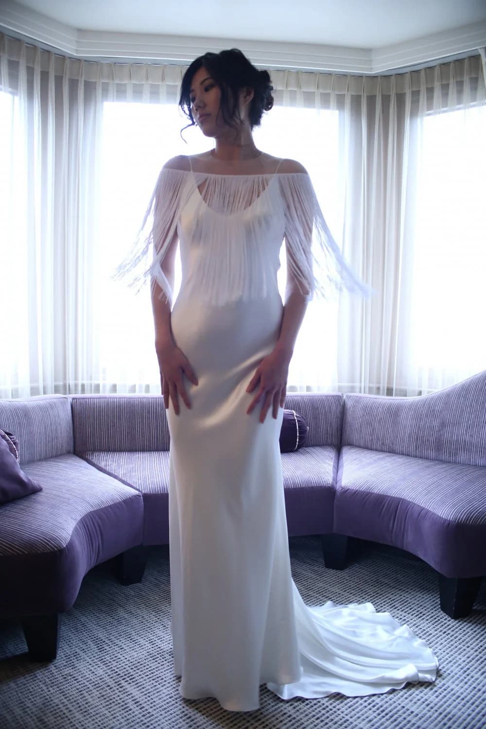 Bride wearing a fringed cape in a bright room.