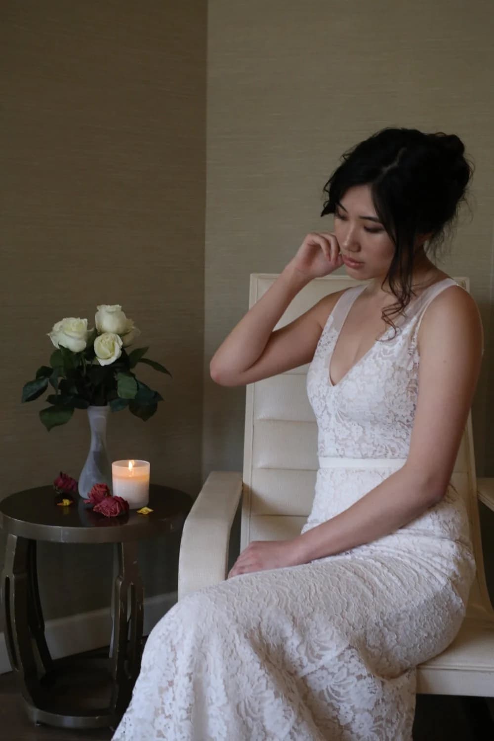 Bride seated beside roses in a lace gown.
