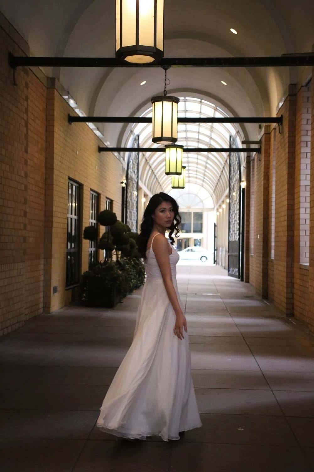 Bride walking through a lit arcade in a white gown.