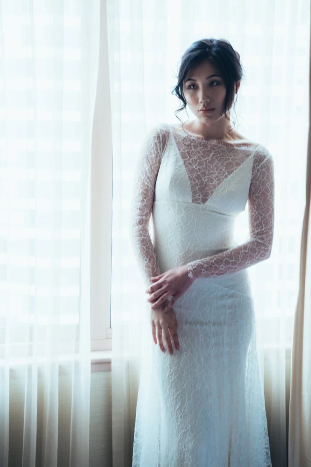 Bride in a lace gown by a bright window.