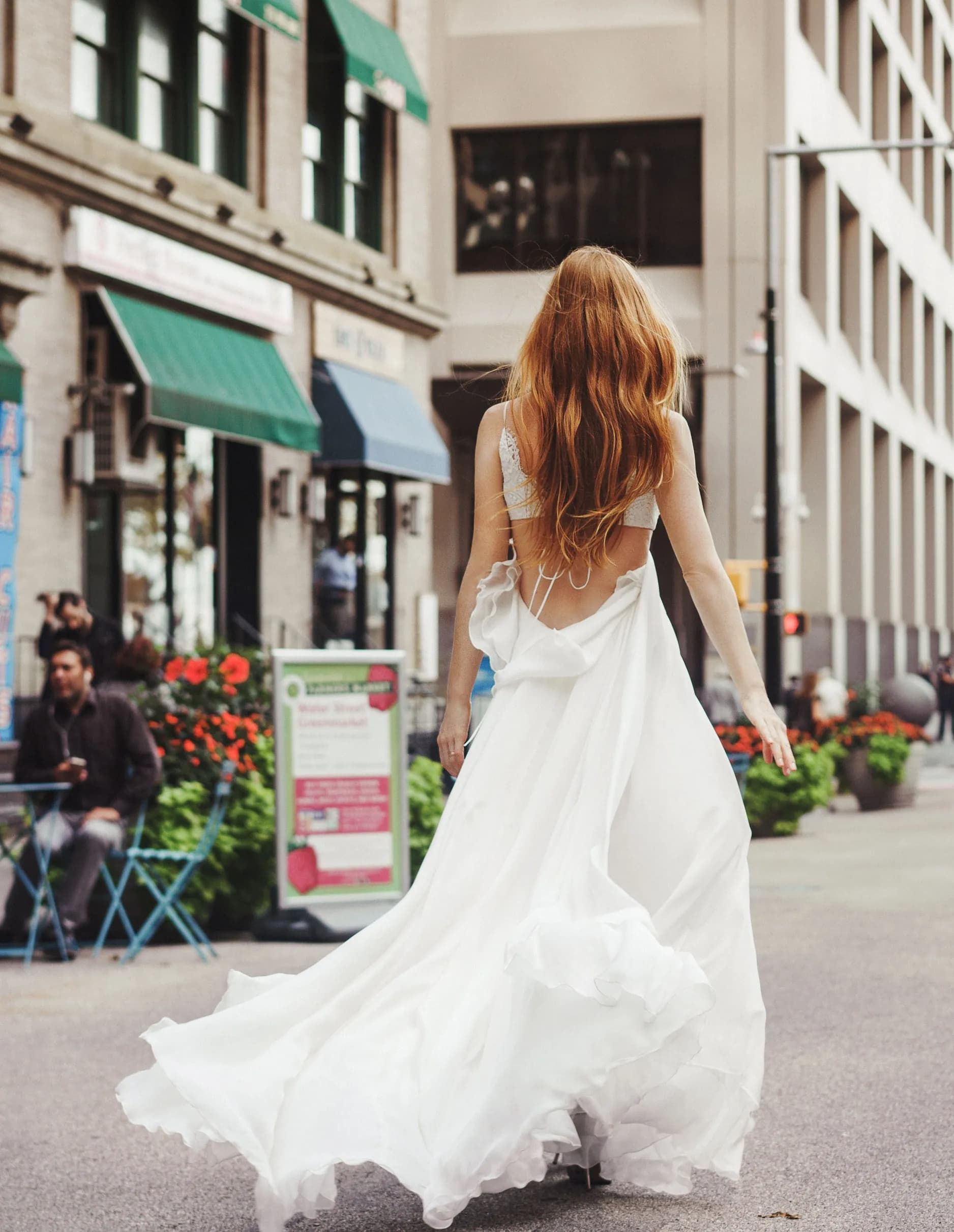 Bride viewed from behind in a white gown on a city street.