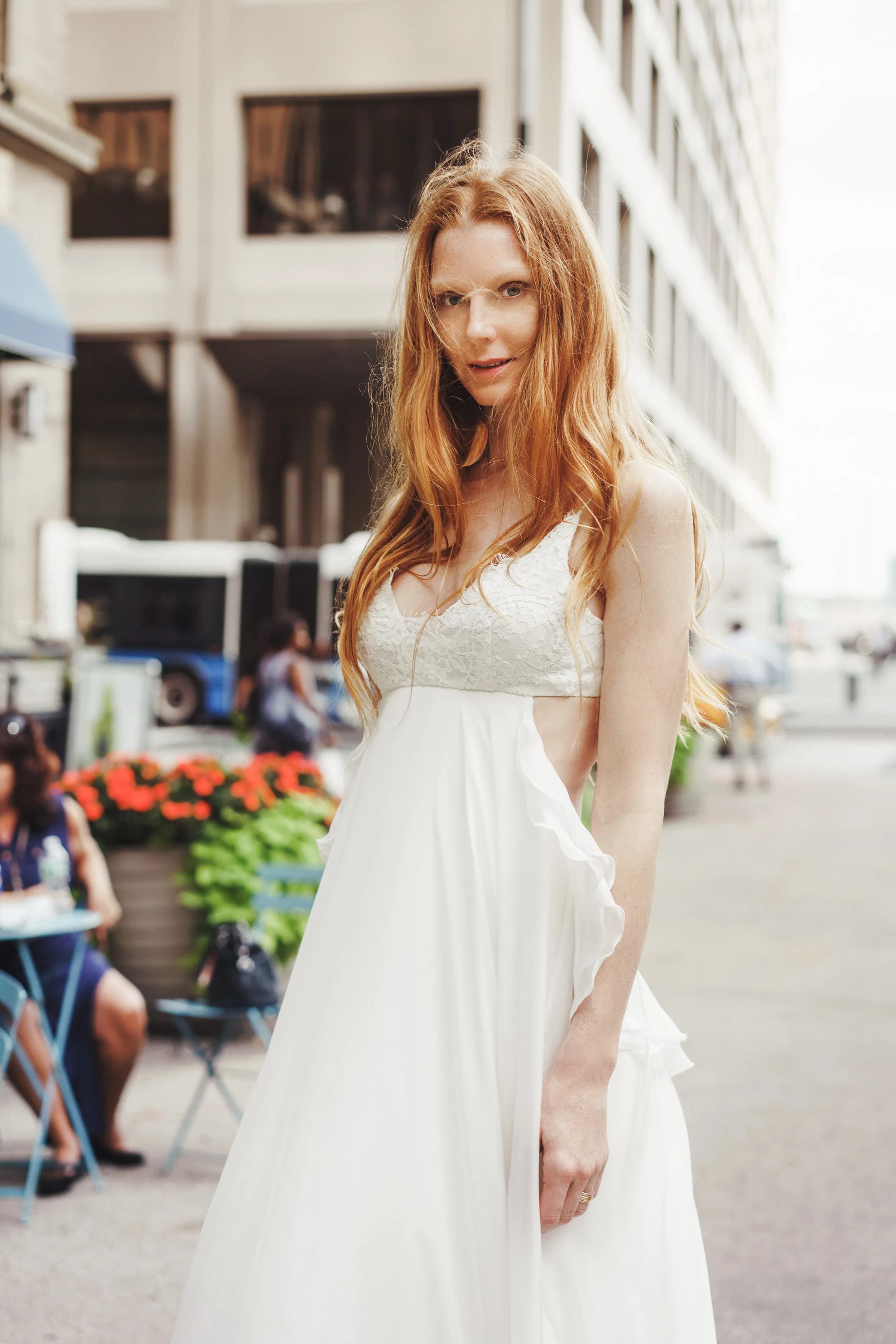 Close portrait of a bride in a white lace gown on a city street.