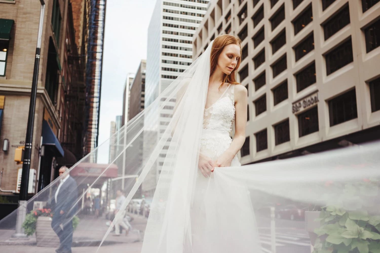 Veiled bride in a white gown walking along a city street.