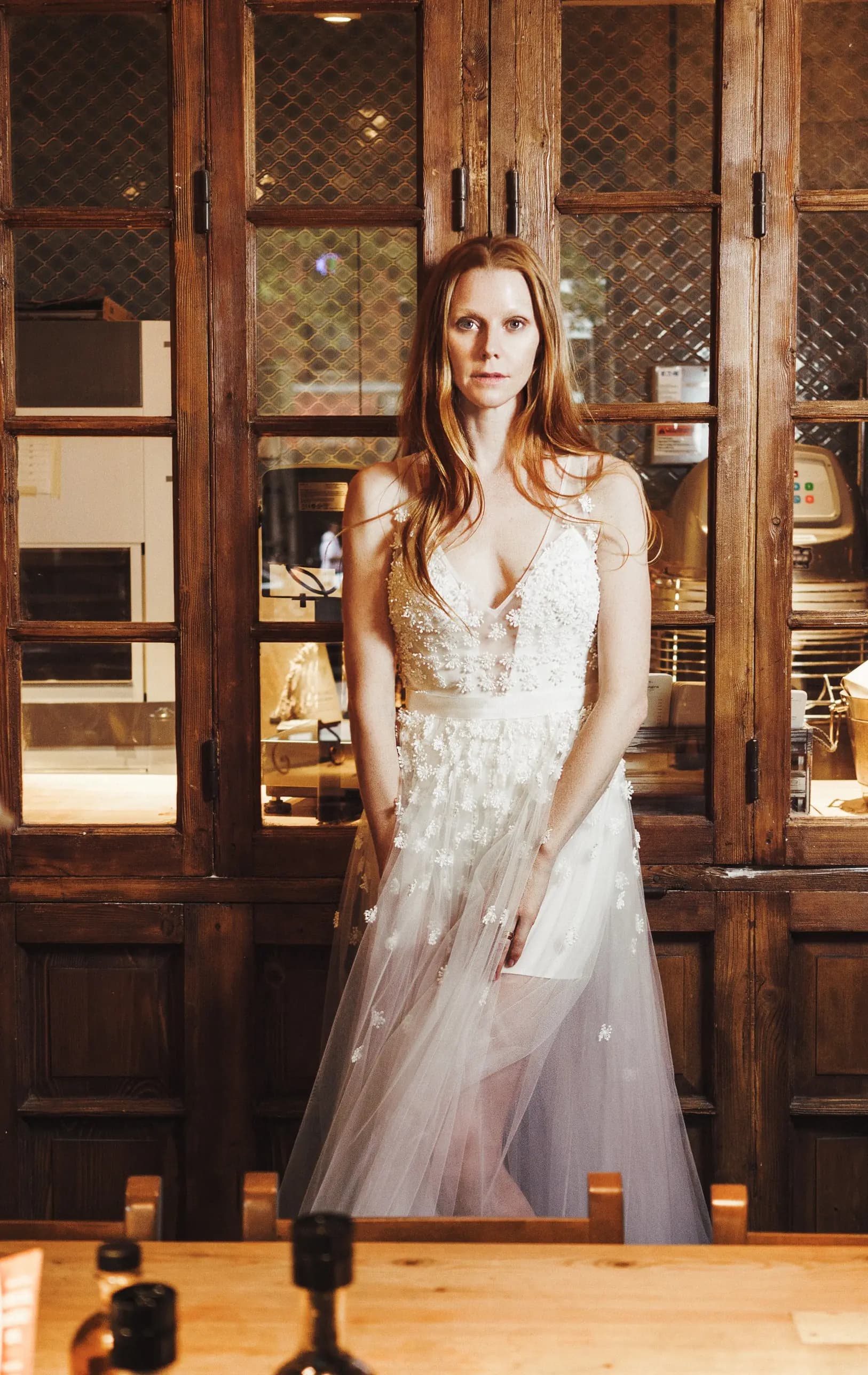 Bride in a floral lace gown standing before wooden doors.