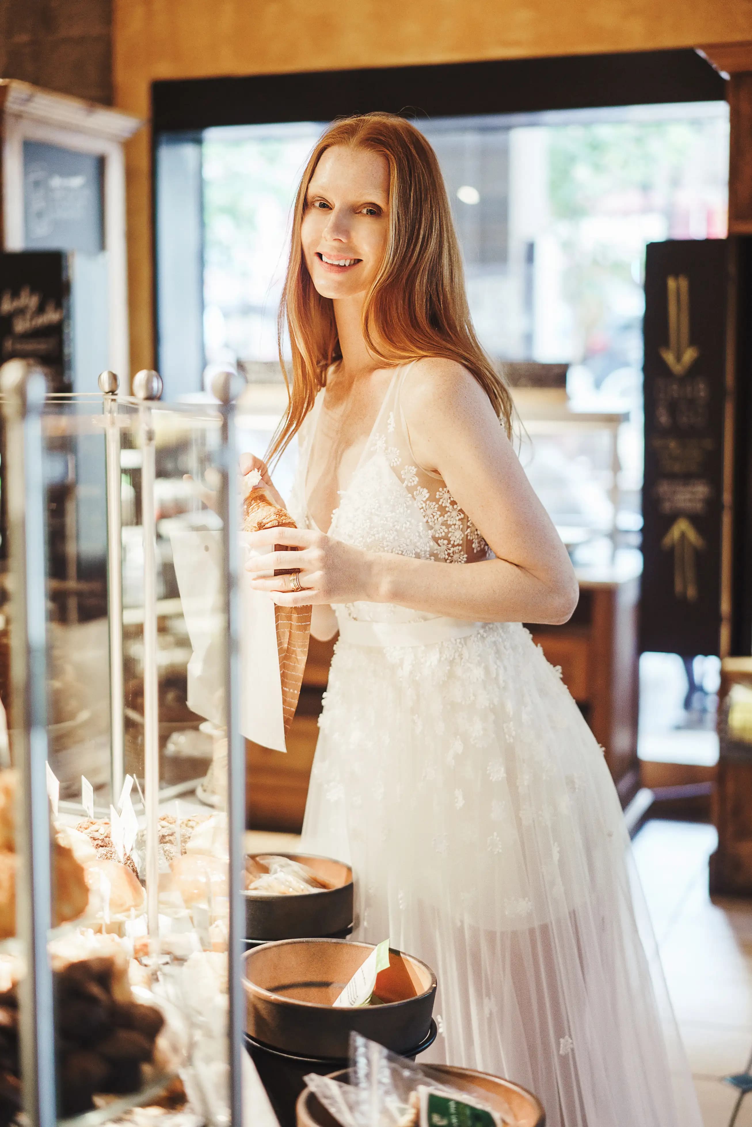 Smiling bride in a floral gown inside a bright shop.