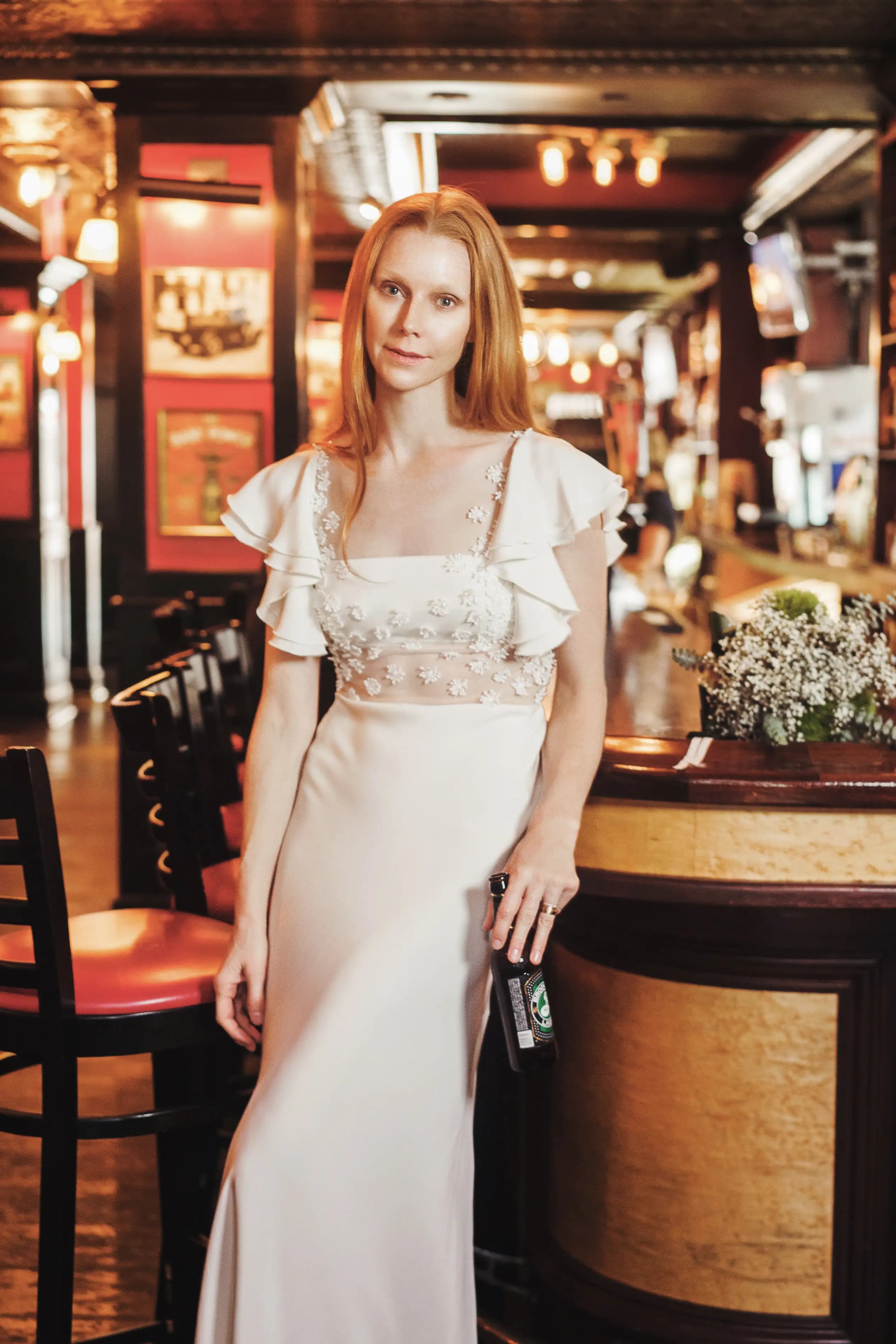 Close portrait of a bride in a ruffled-sleeve gown at a bar.