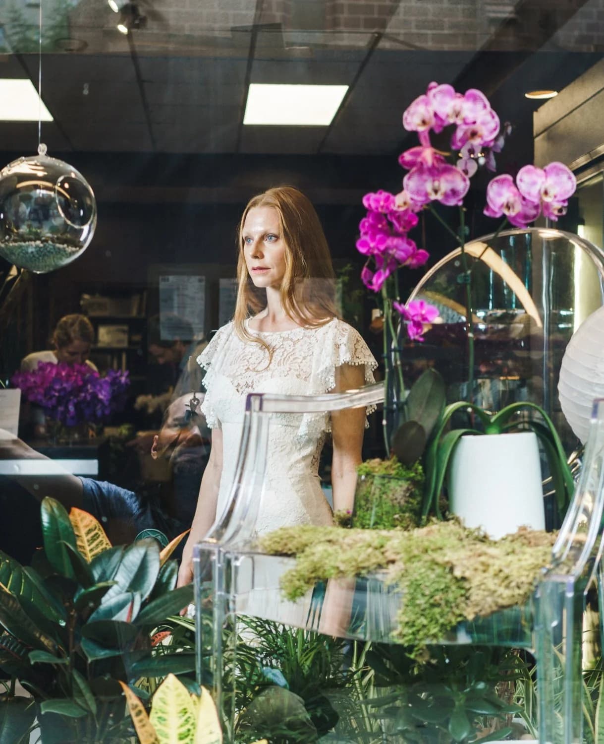 Bride in a lace gown among orchids and indoor plants.