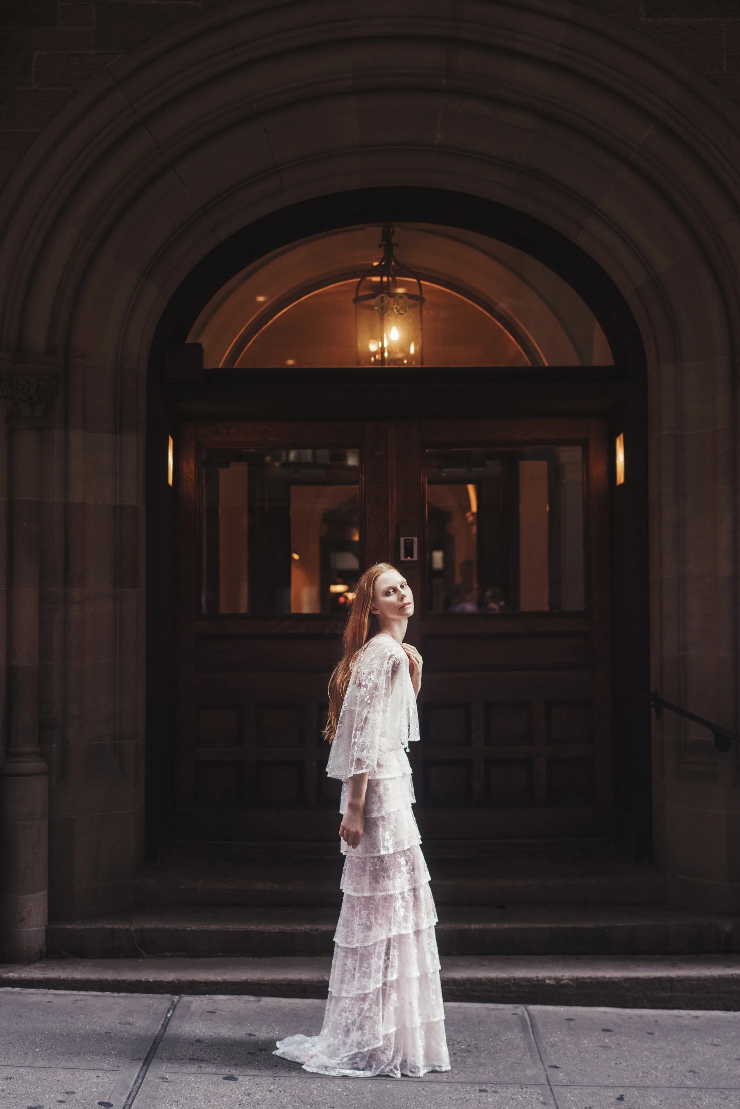 Bride in a tiered lace gown before a dark doorway.