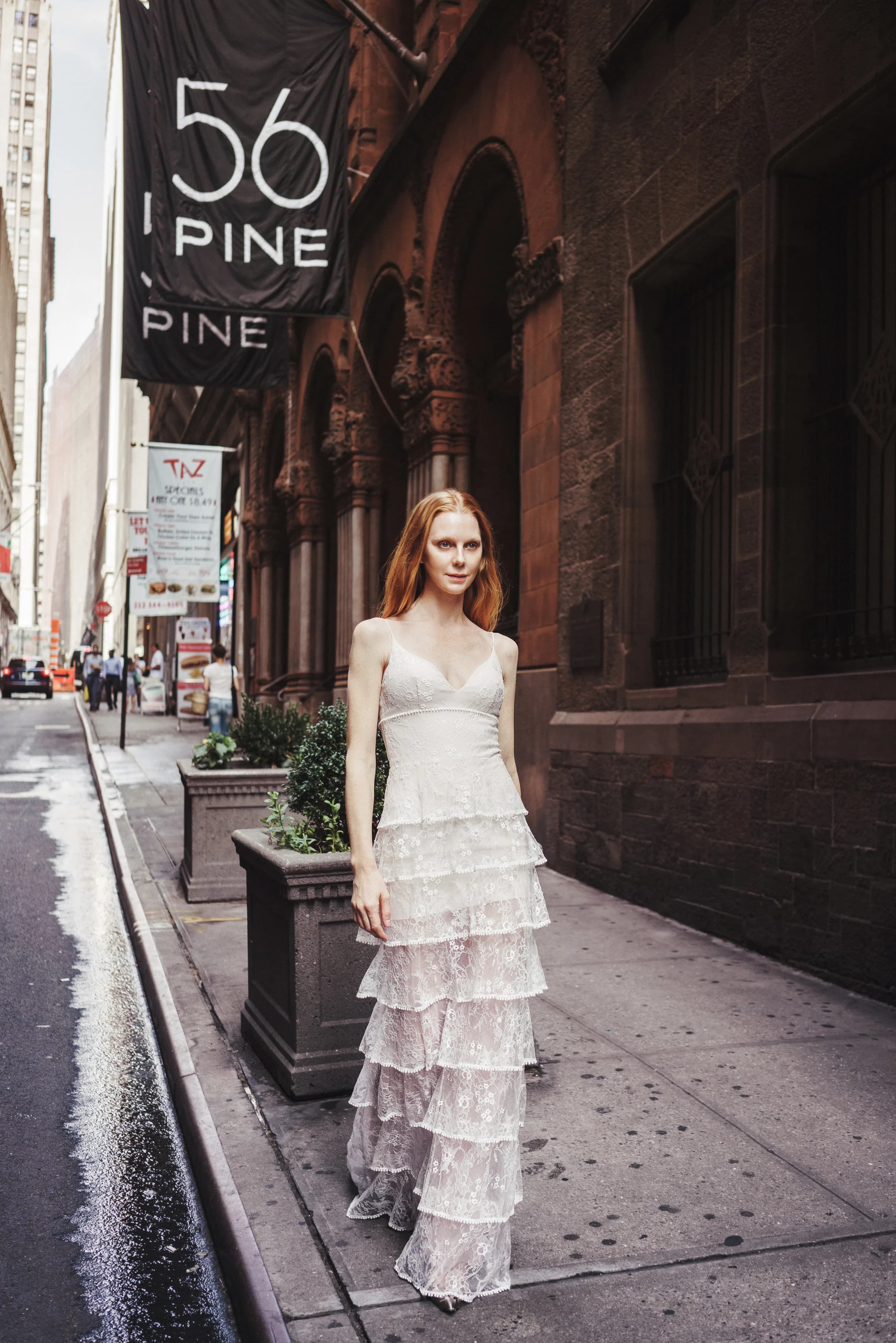 Bride in a tiered lace gown on a city sidewalk.