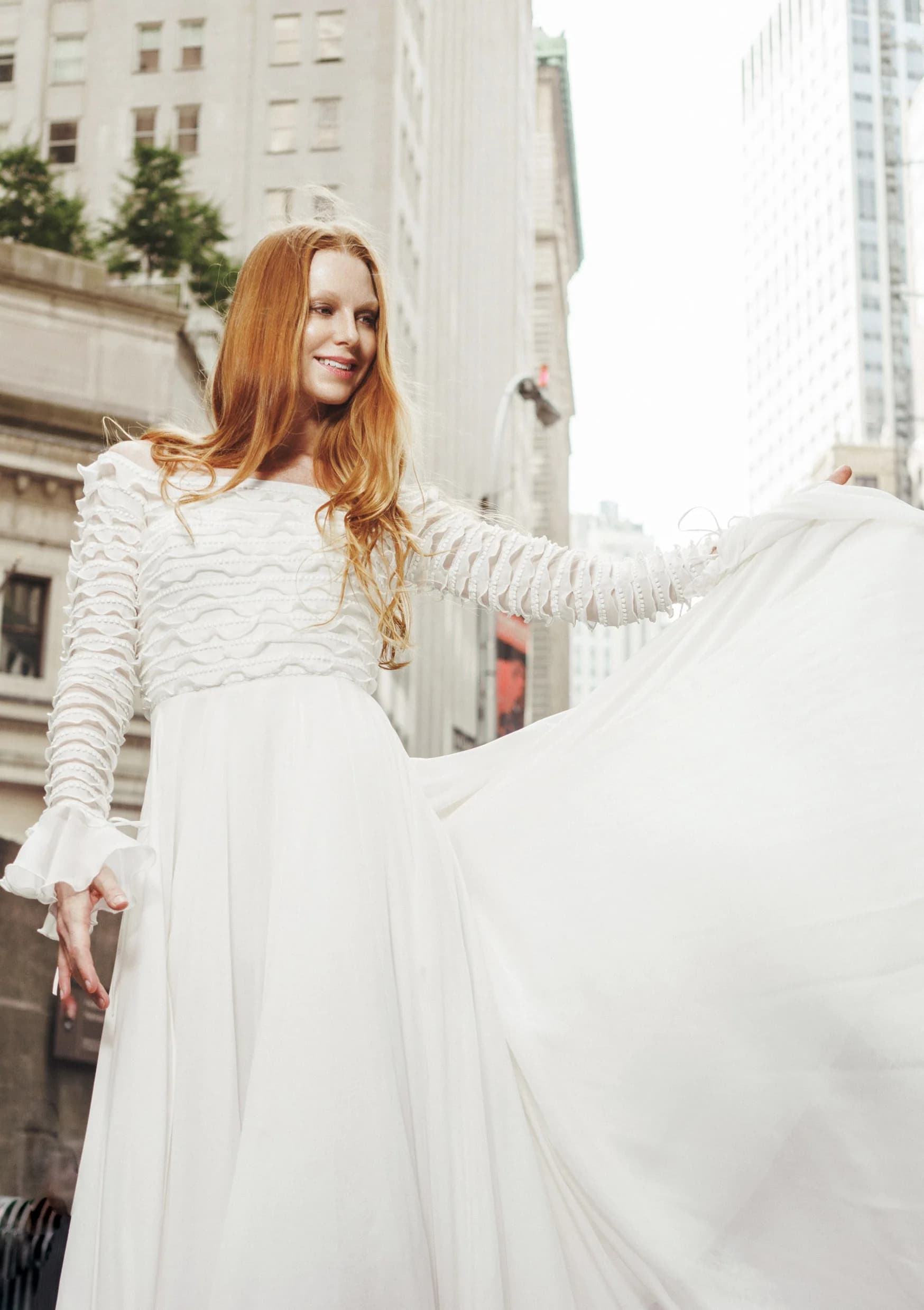 Bride lifting a full white skirt between downtown buildings.