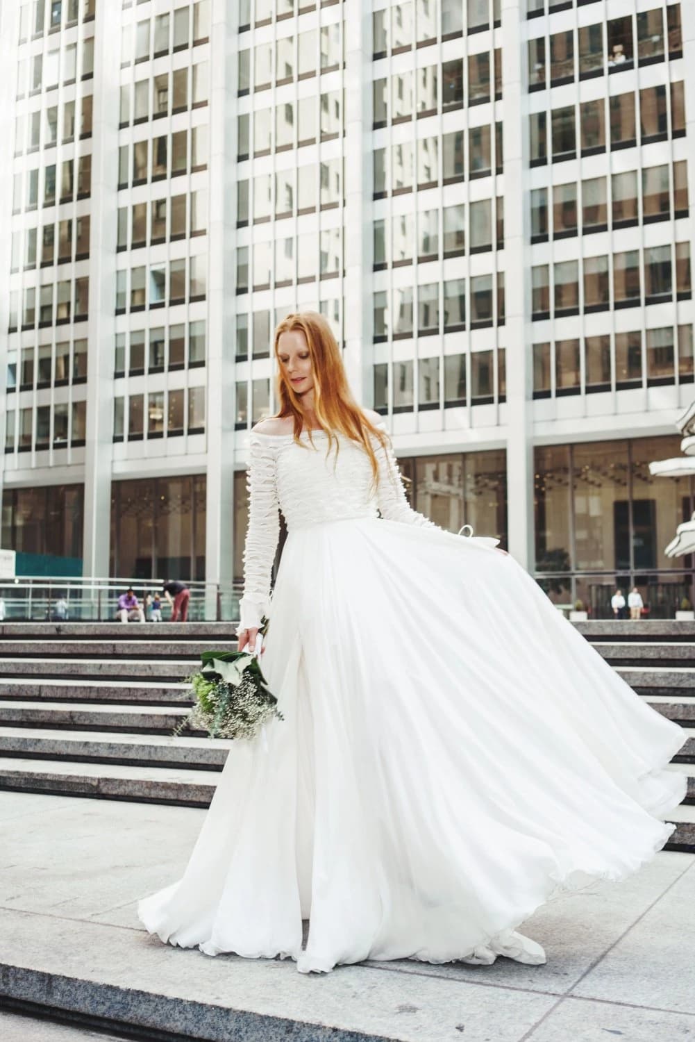 Bride holding a bouquet on broad city steps.