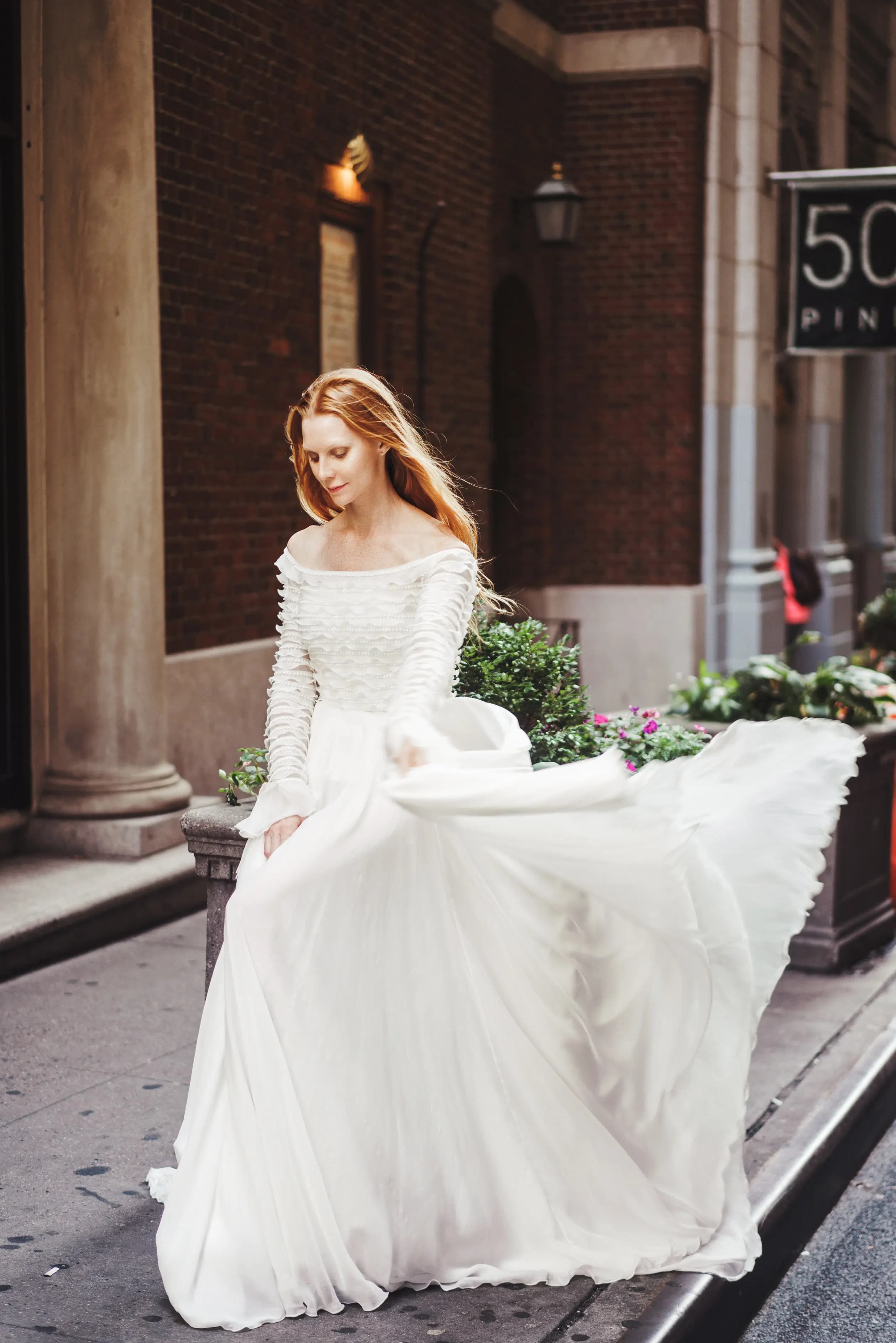 Bride lifting a flowing skirt beside a brick entryway.