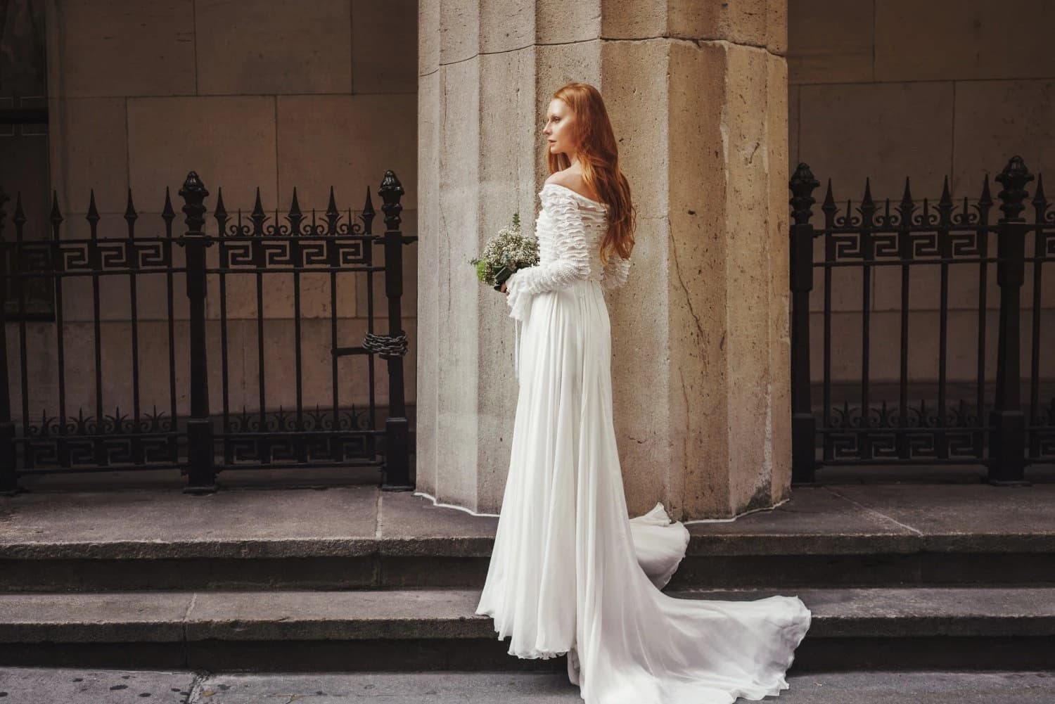 Bride in profile with a bouquet beside stone columns.