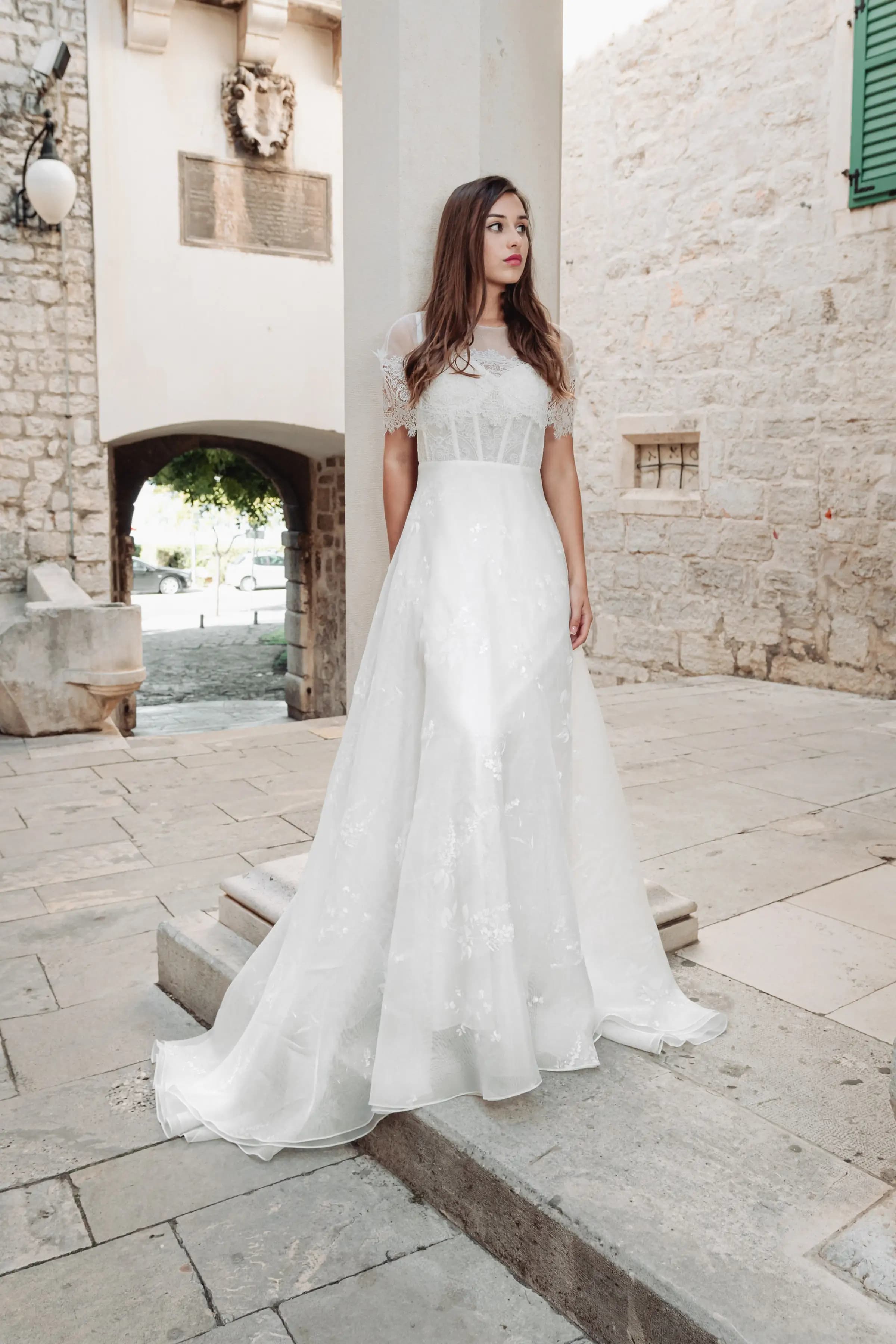 Bride in a lace gown in a stone courtyard.