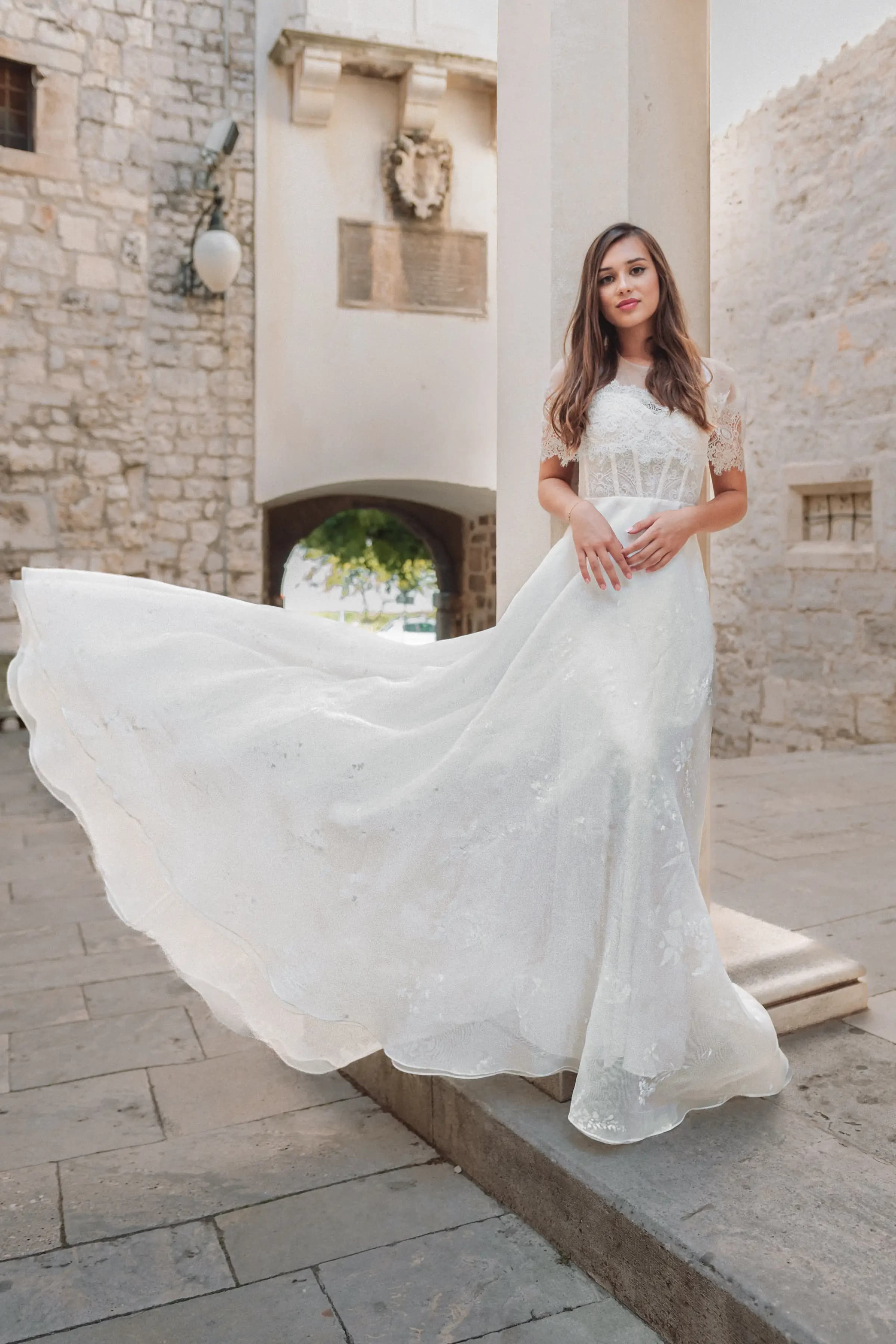 Bride holding a flowing skirt in a stone courtyard.