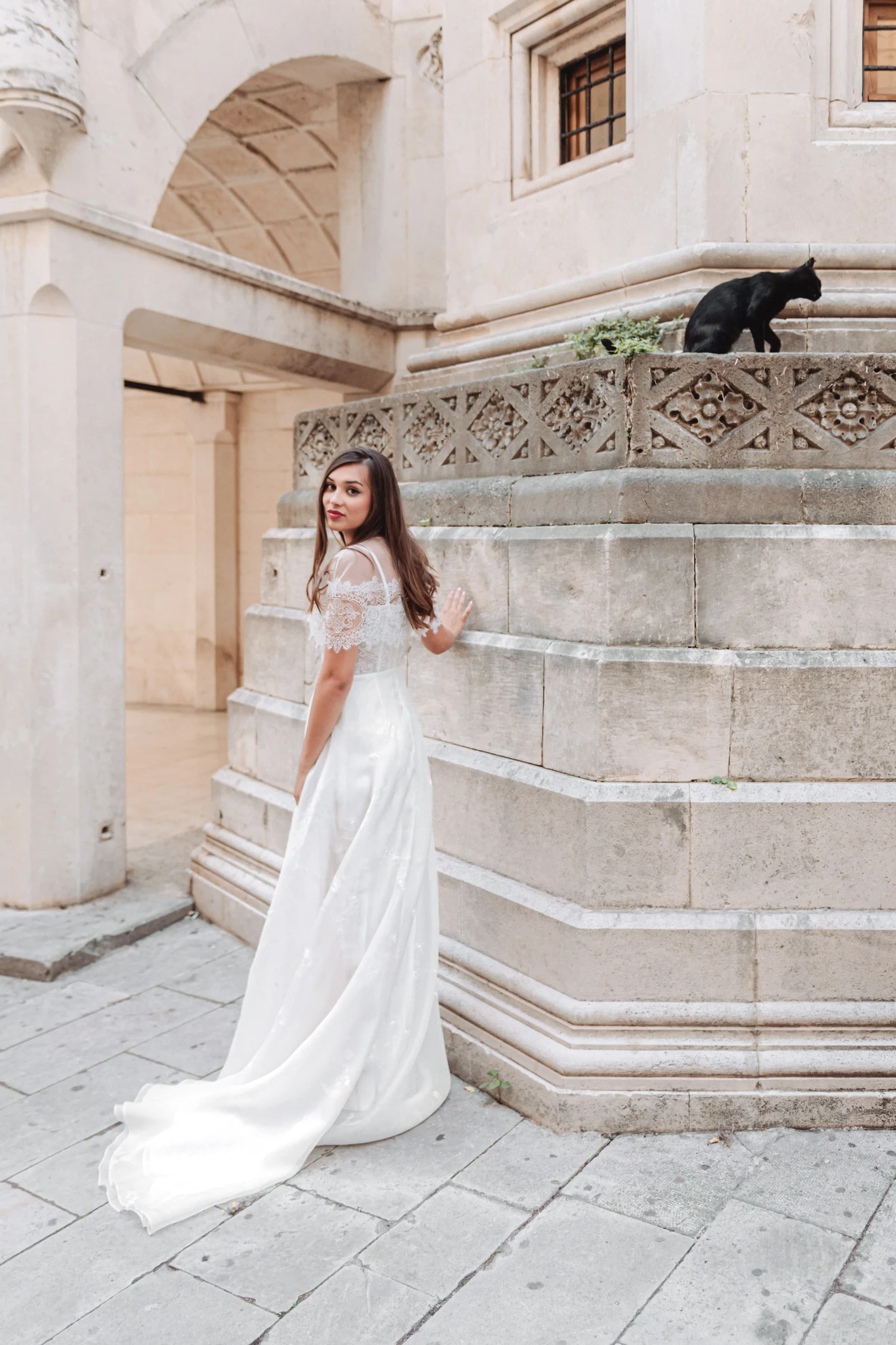 Bride looking back beside a carved stone wall and black cat.