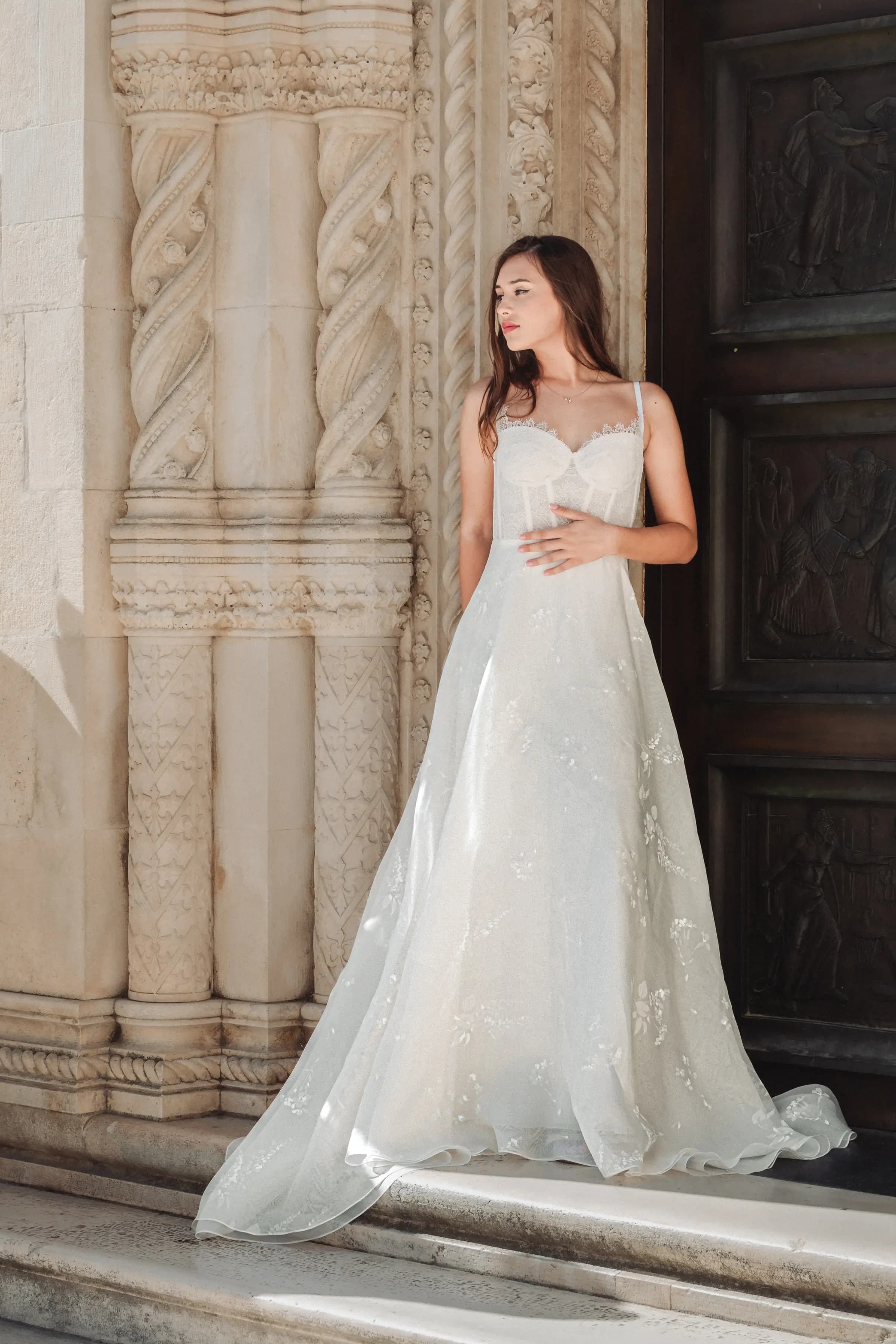 Bride in a white gown beside carved columns and a dark door.