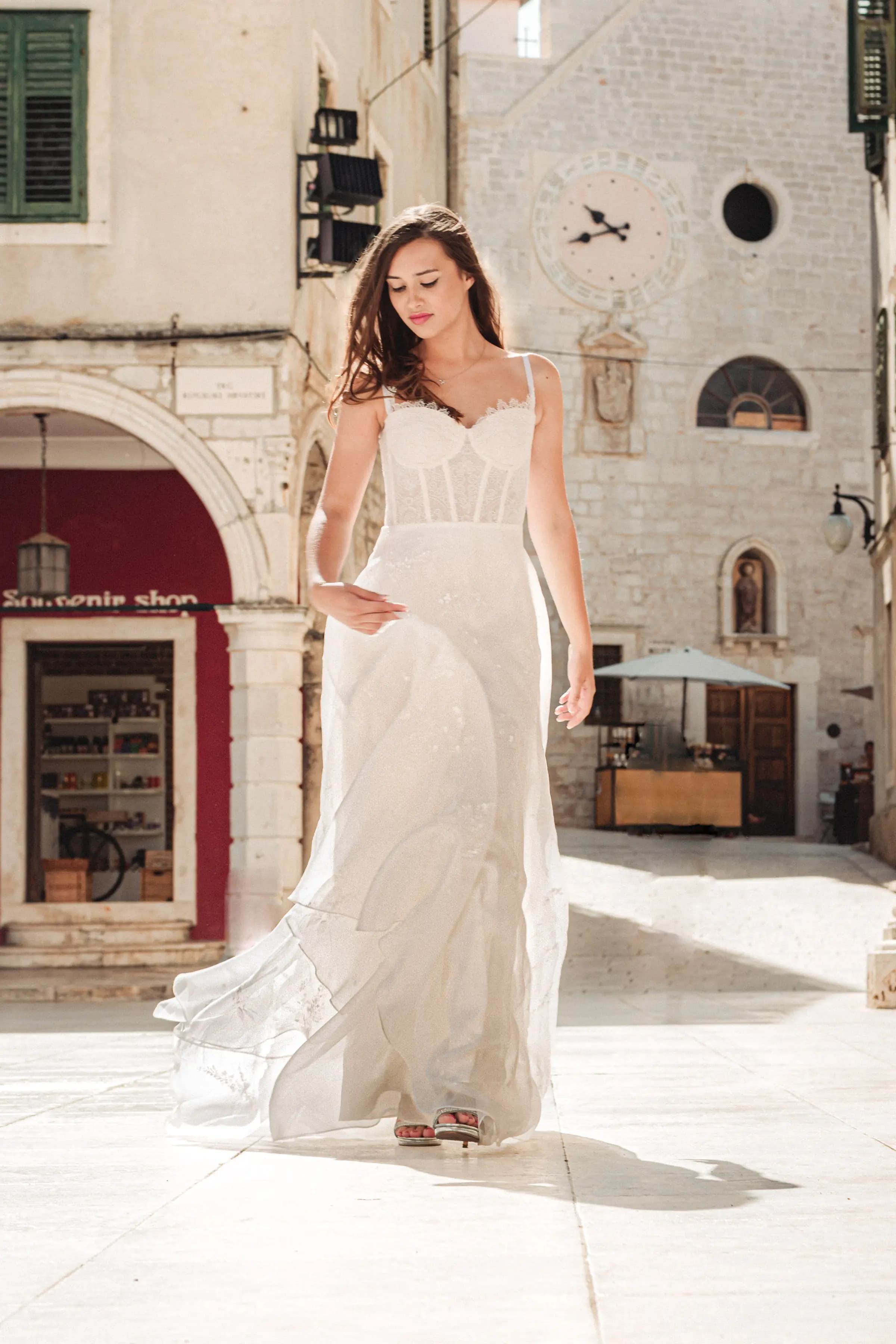 Bride in a white gown in a sunlit stone square.