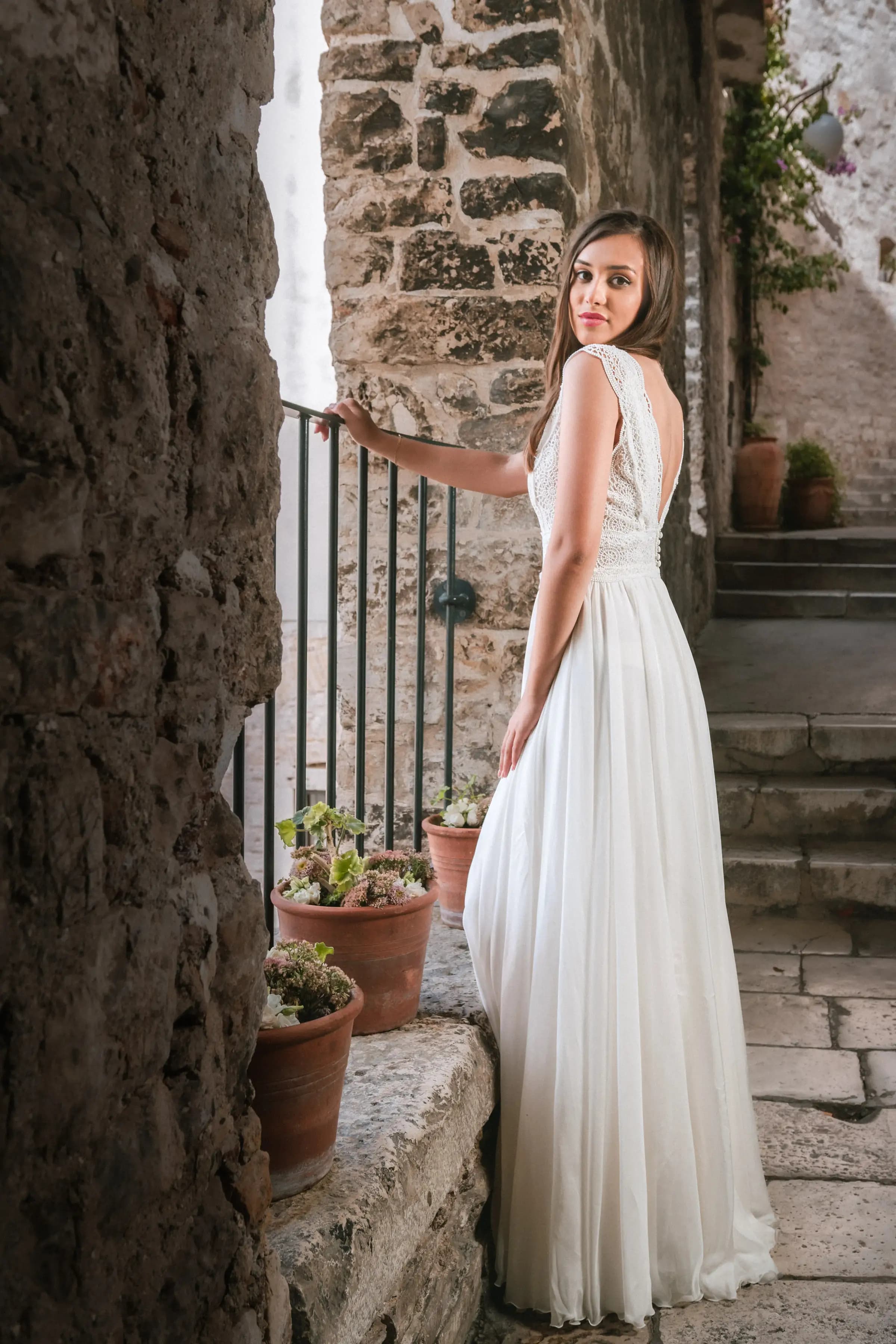 Bride showing the lace back of a gown among stone walls.