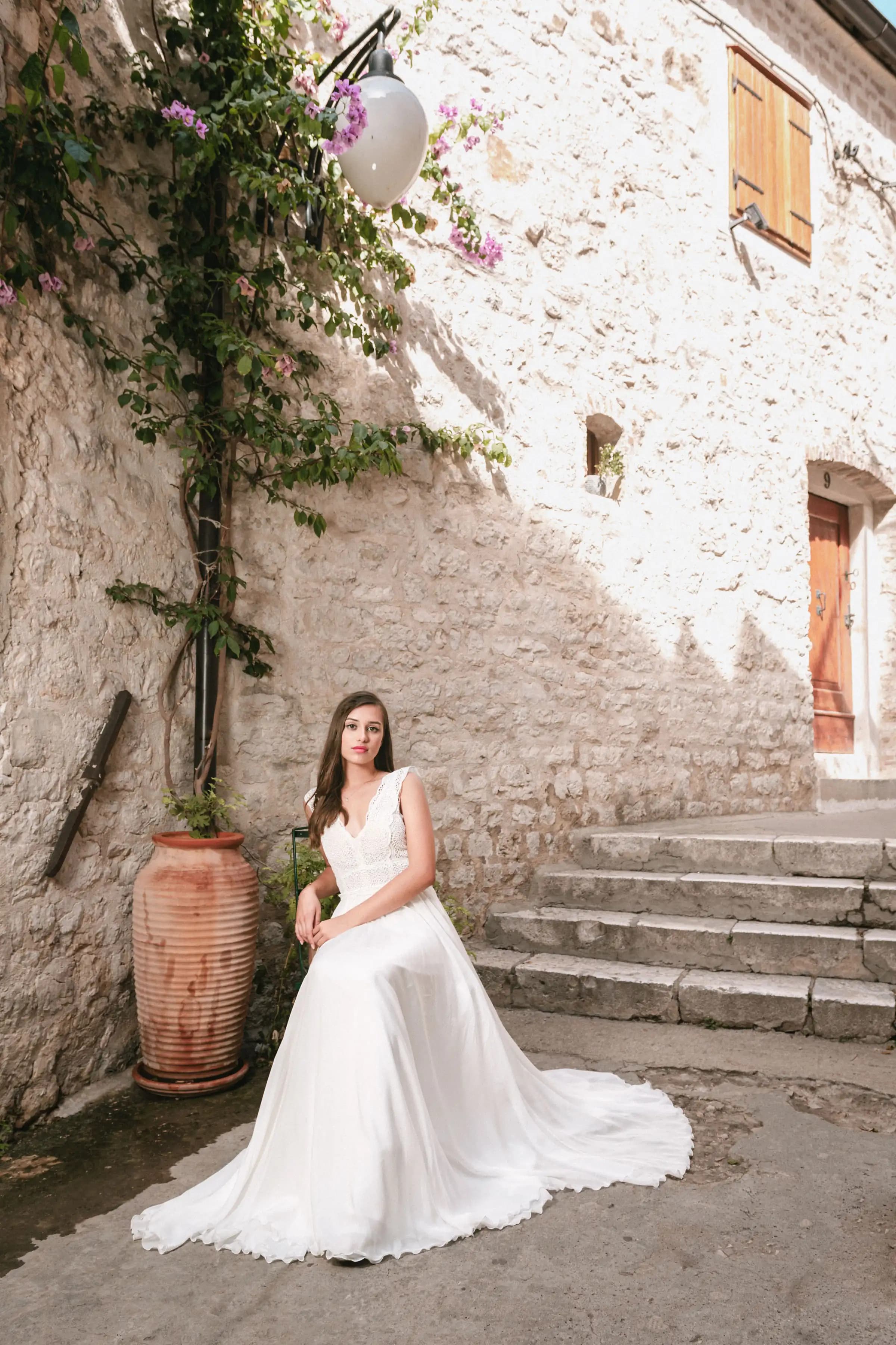 Bride seated on stone steps beside a flowered wall.