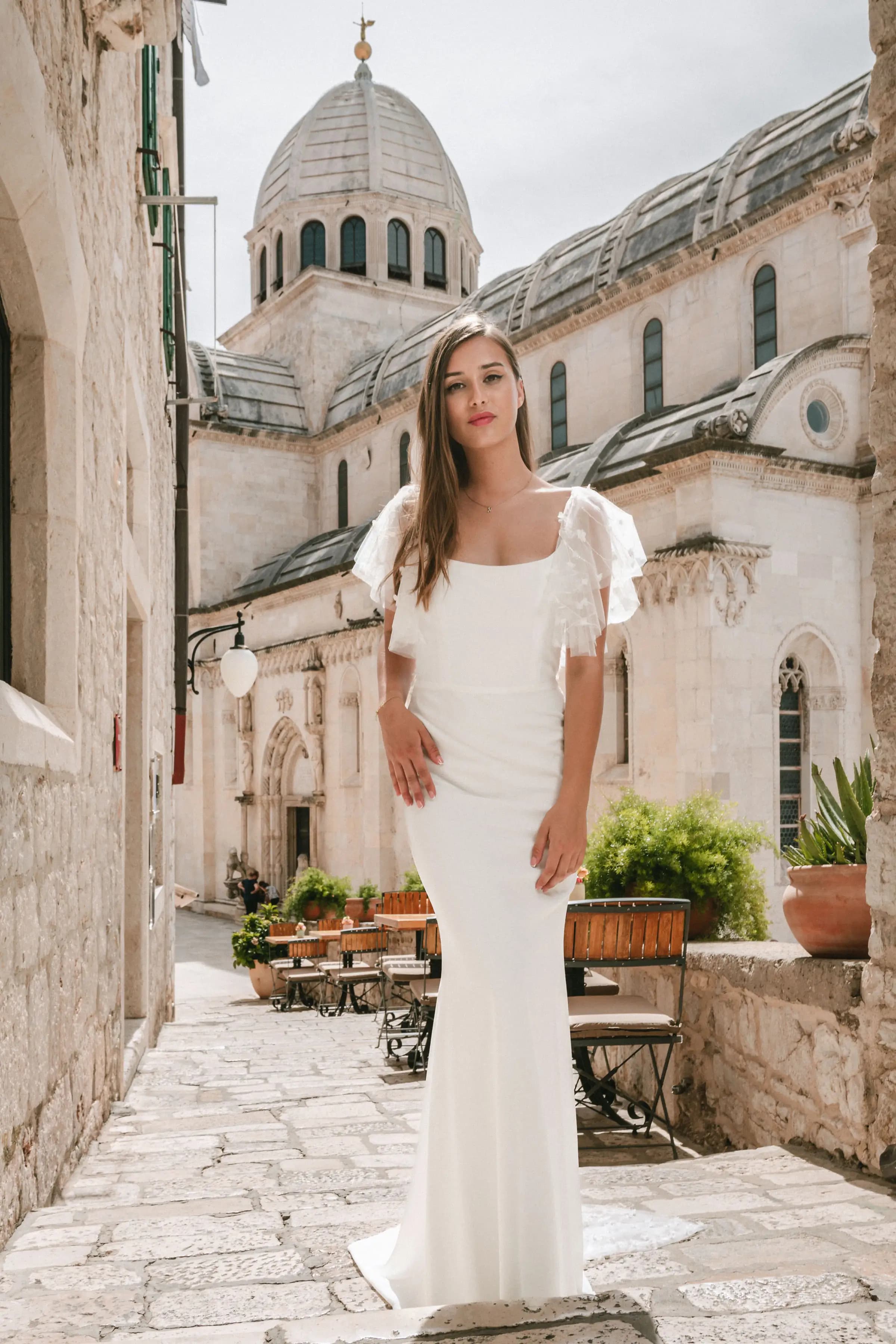 Bride in a fitted gown before a domed stone church.