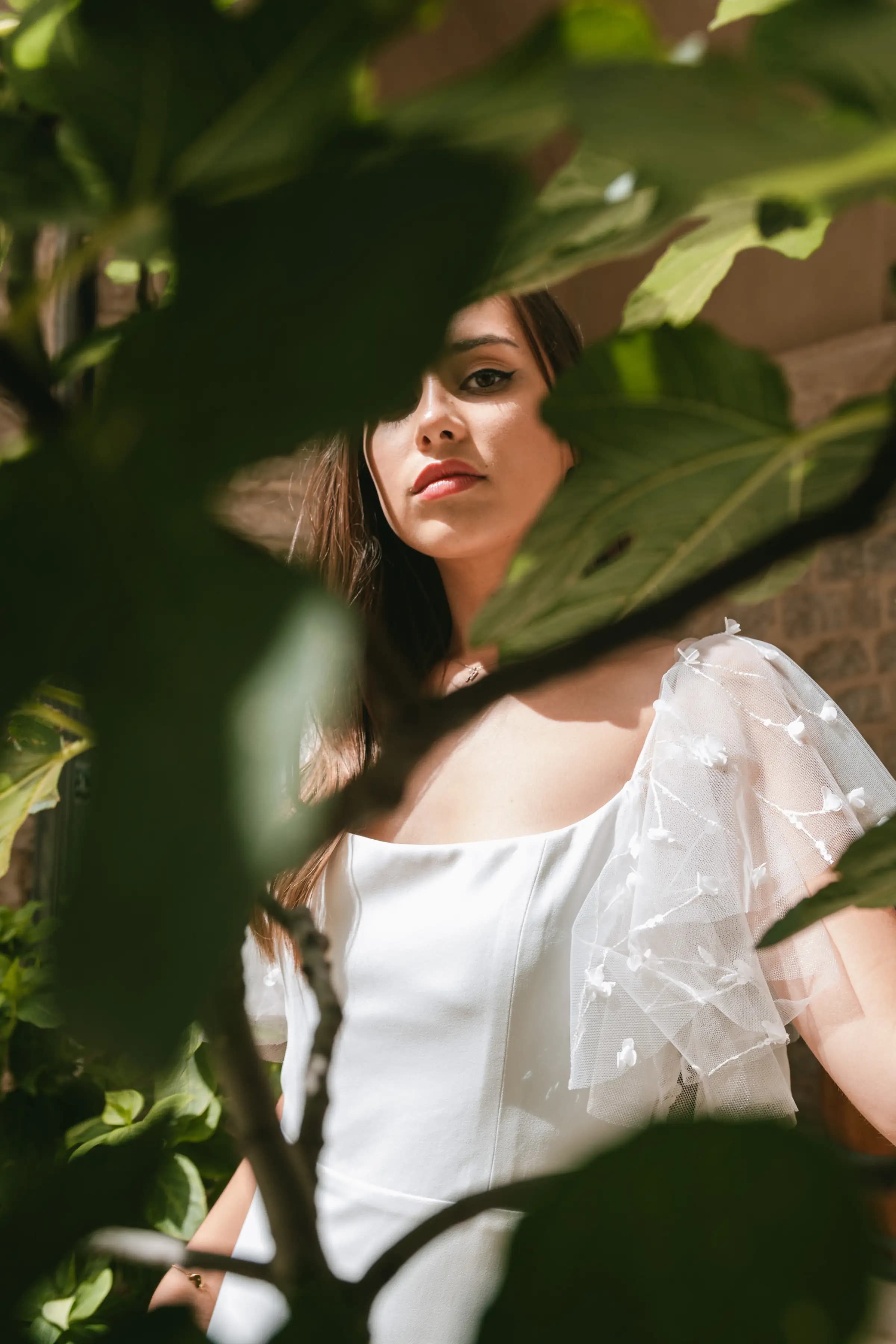 Bride partly framed by leaves in a white gown.