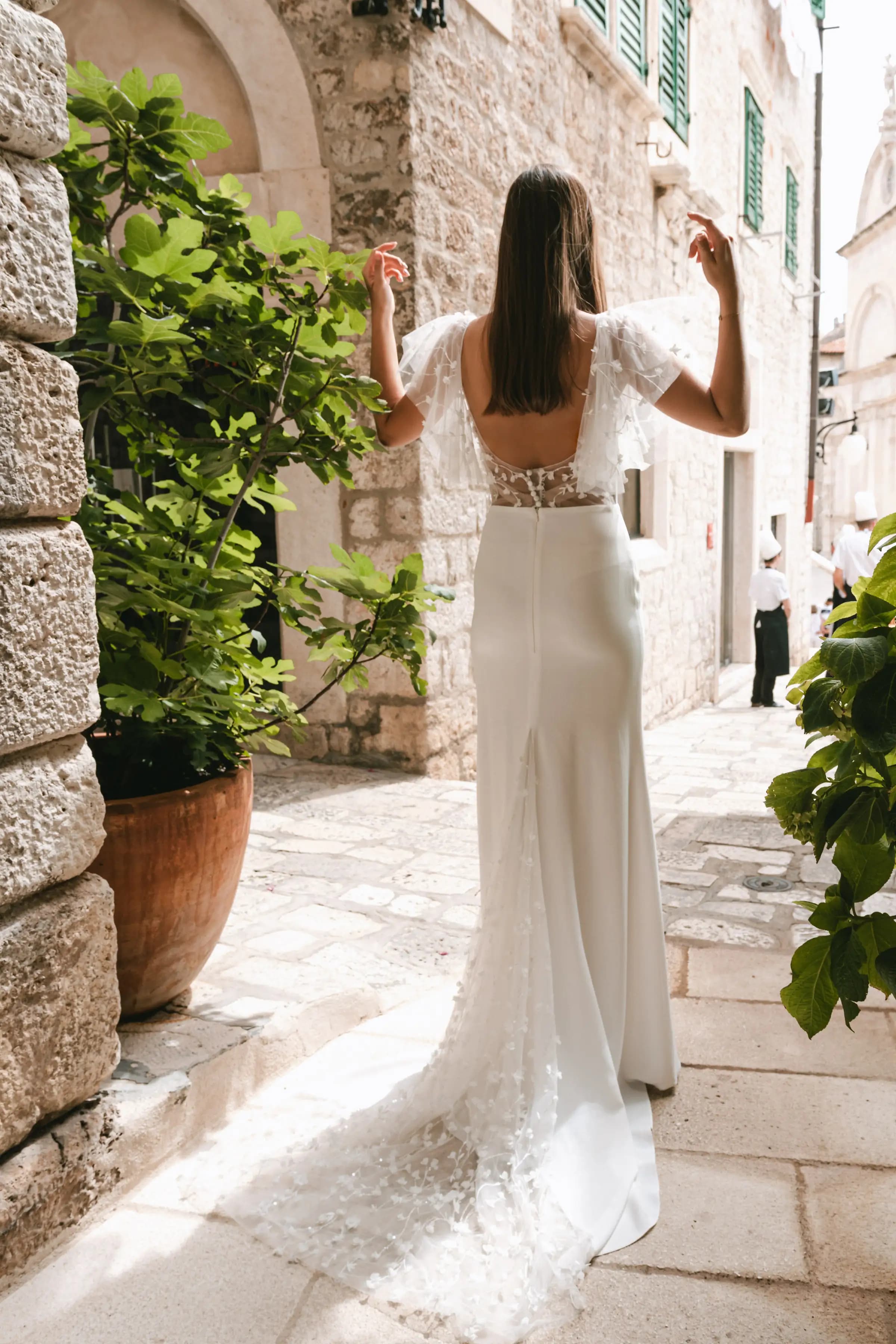 Bride viewed from behind in a gown with sheer sleeves.