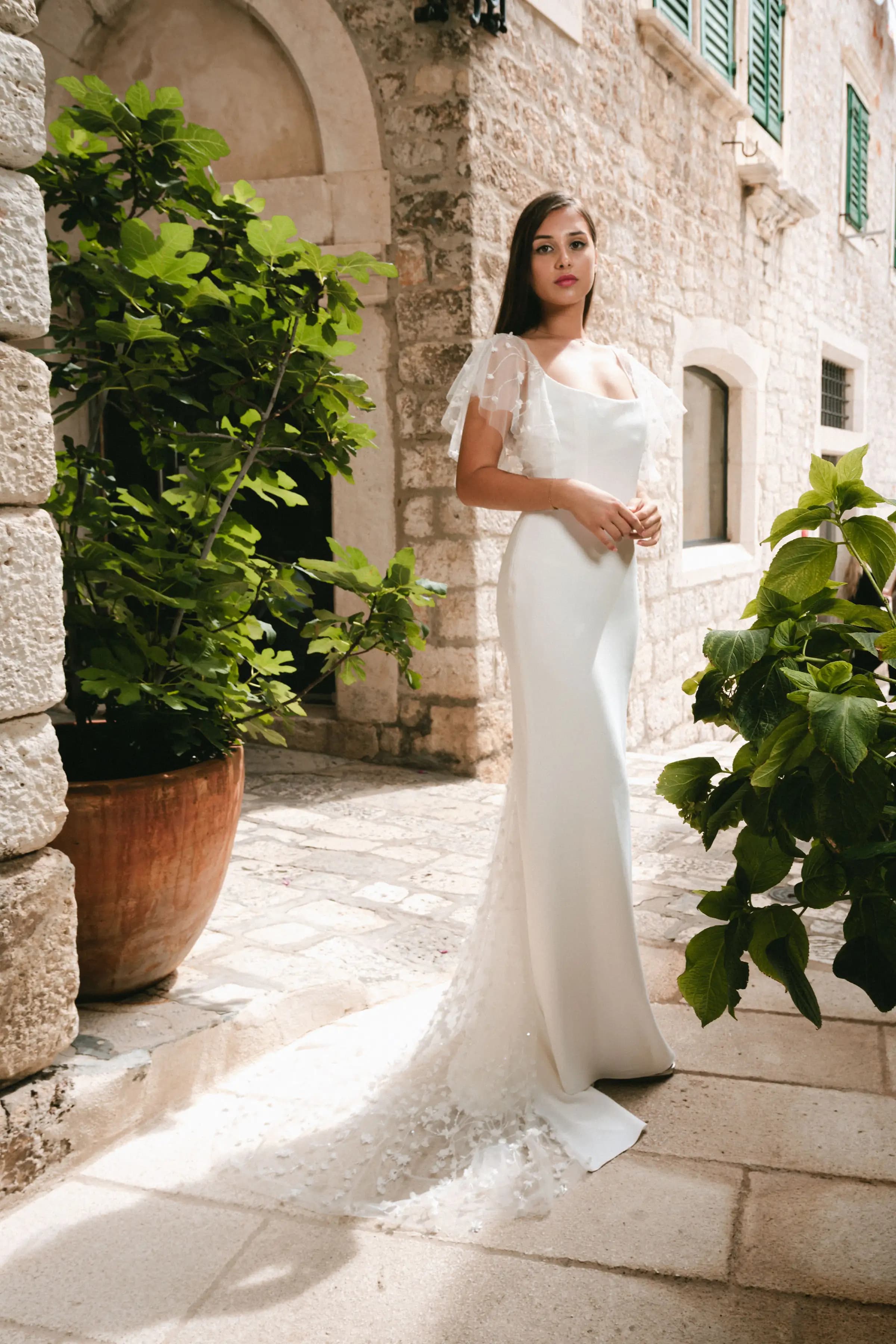 Bride in a fitted gown among leafy stone courtyards.