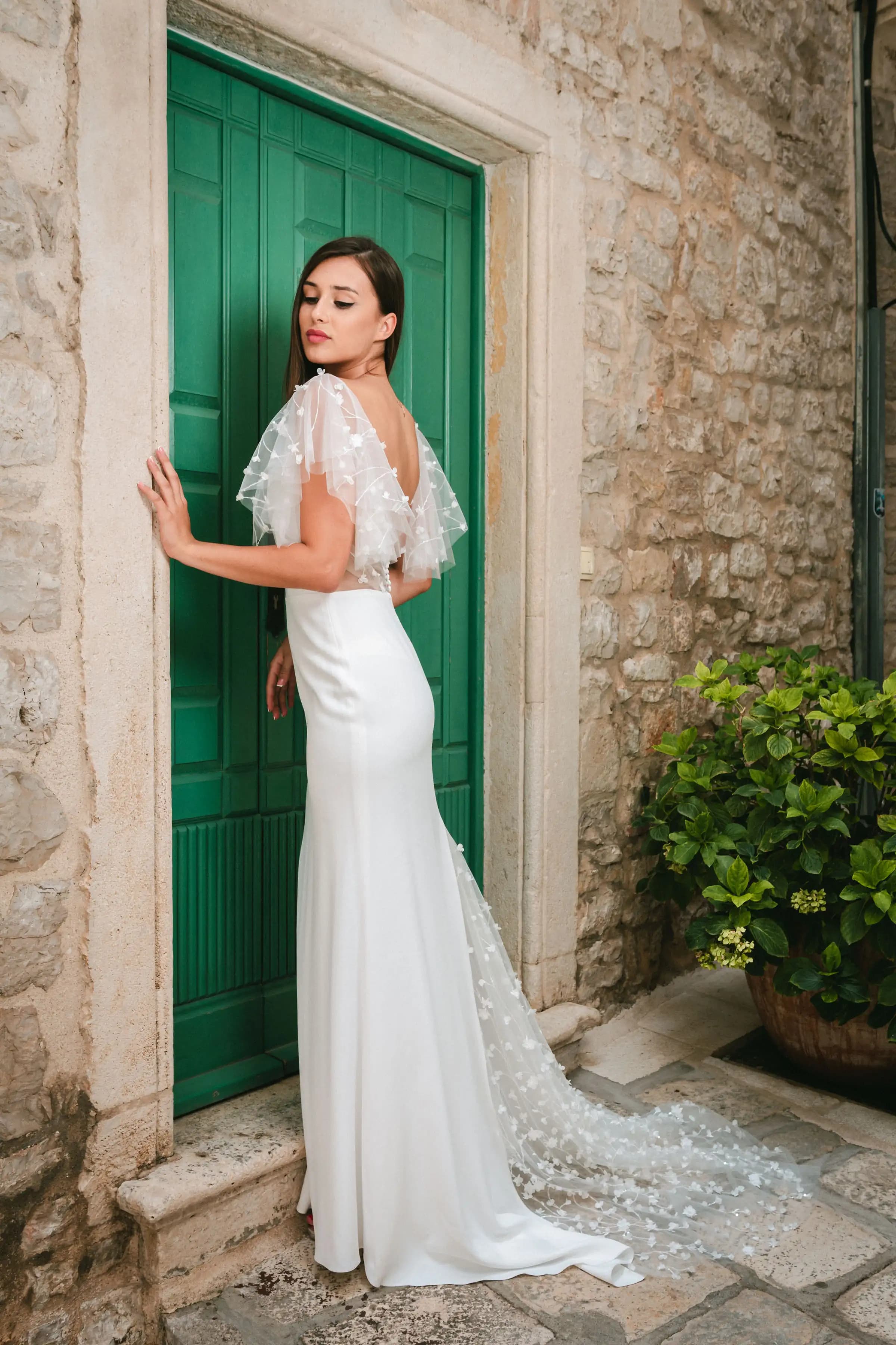 Bride showing the back of a sheer-sleeve gown by a green door.