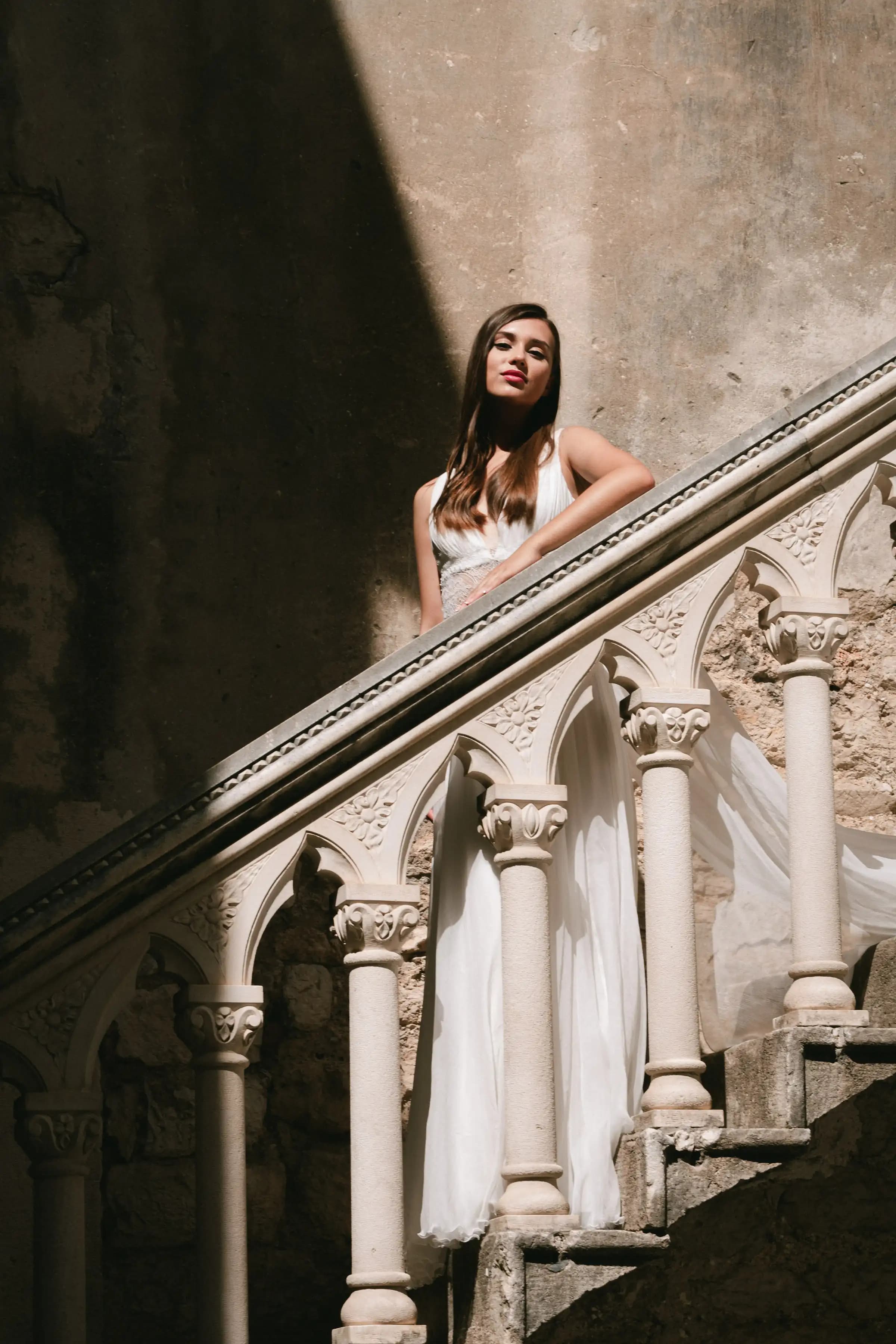 Bride on a carved stone staircase in a flowing gown.