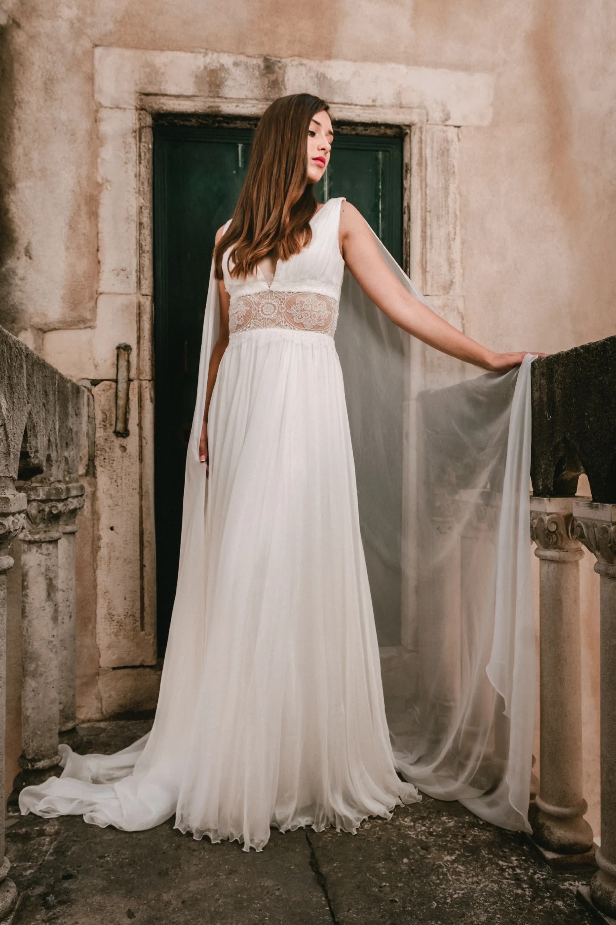 Bride holding a veil beside a dark green doorway.