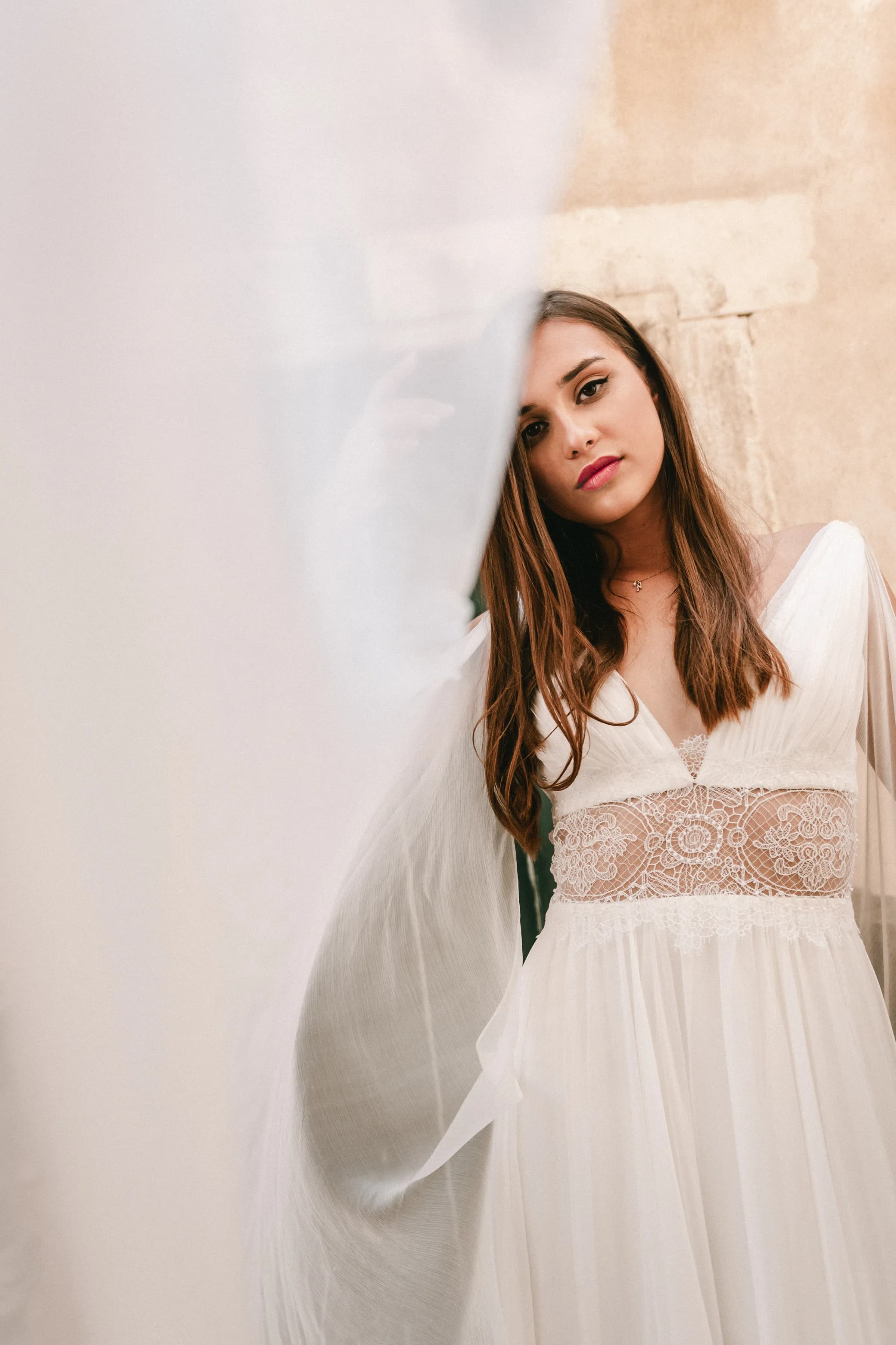 Close portrait of a bride partly veiled in a lace gown.
