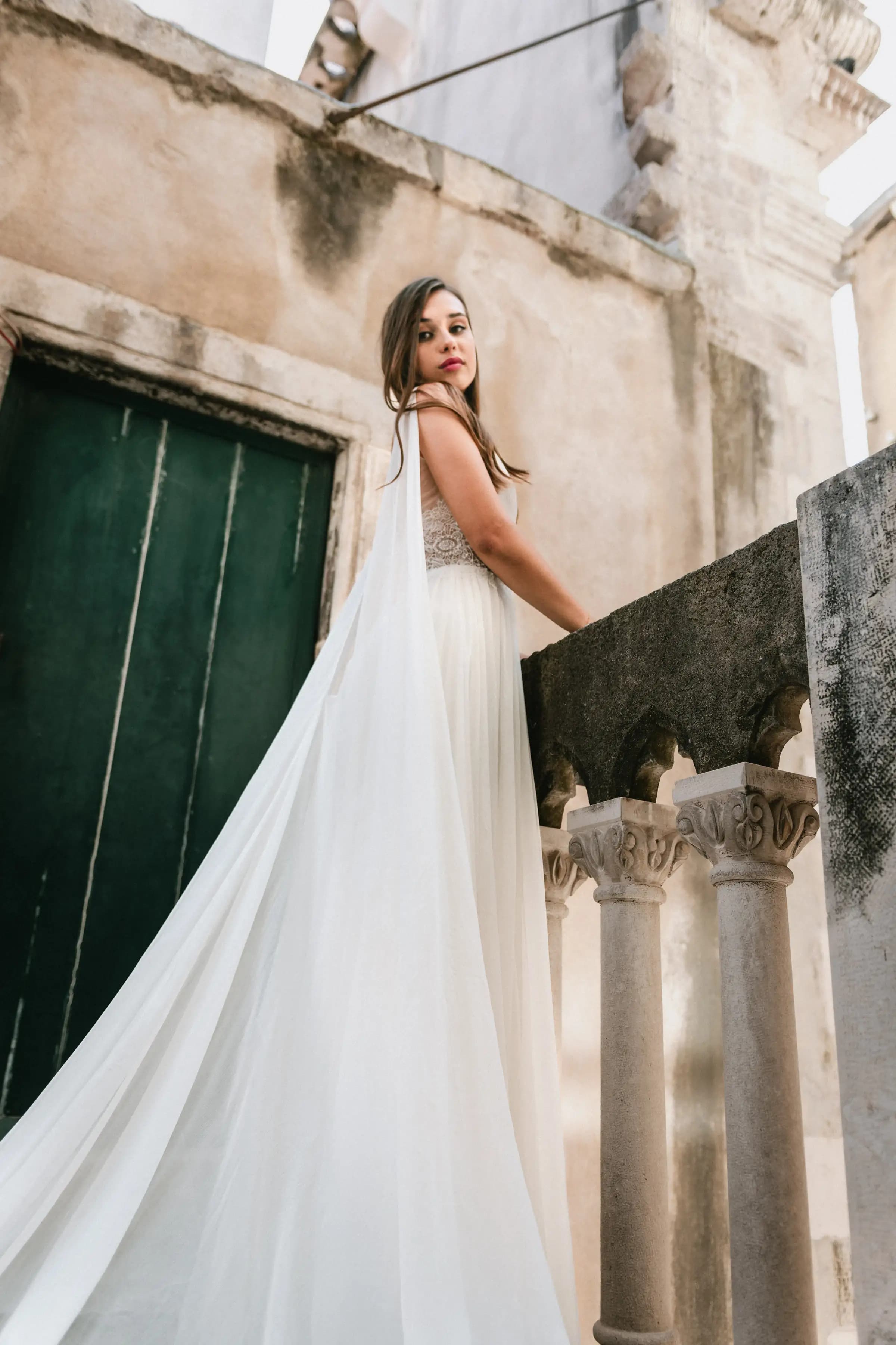 Bride looking back on a stone staircase with a long veil.