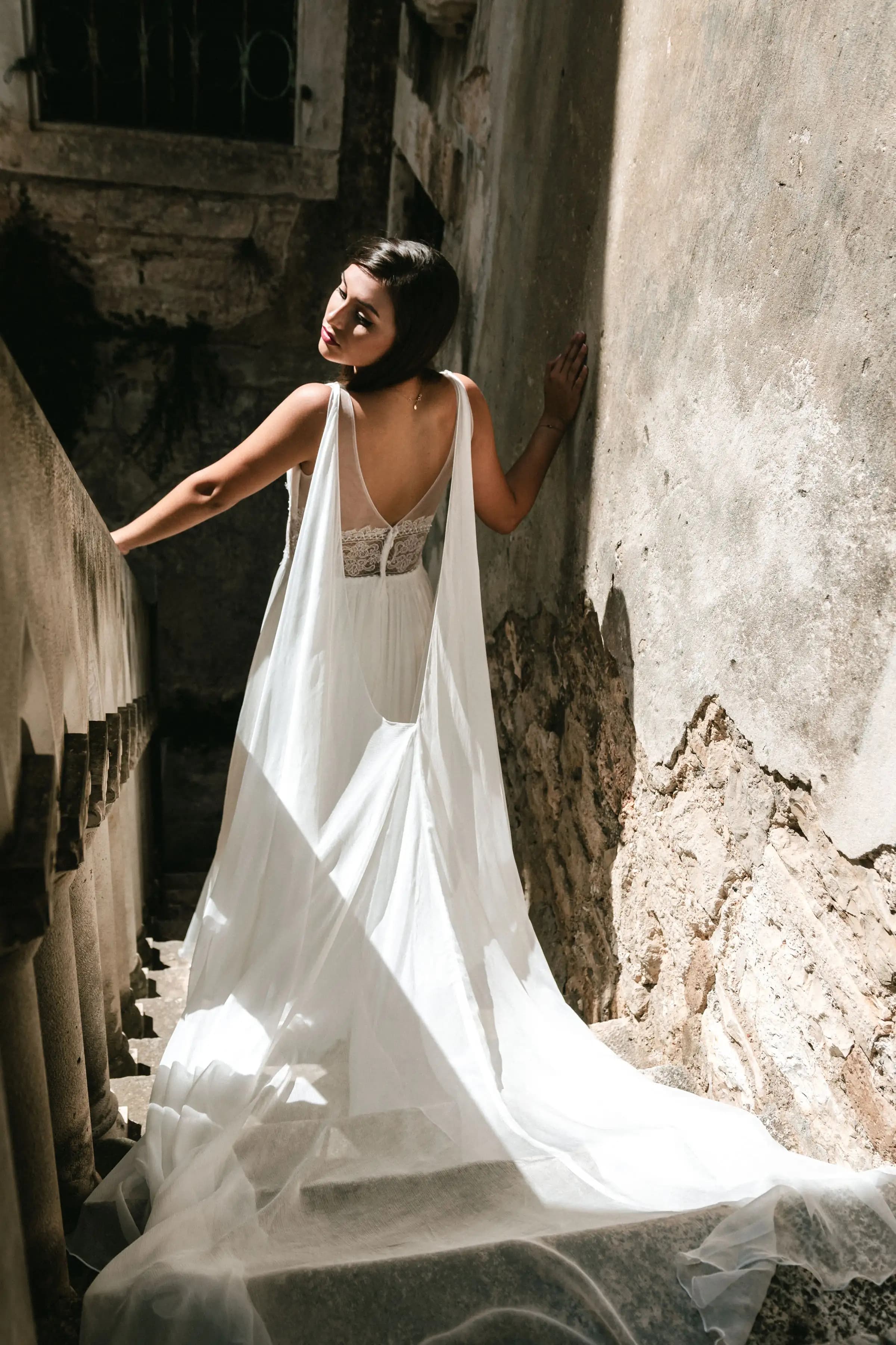 Bride showing the open back of a gown on a narrow stairway.