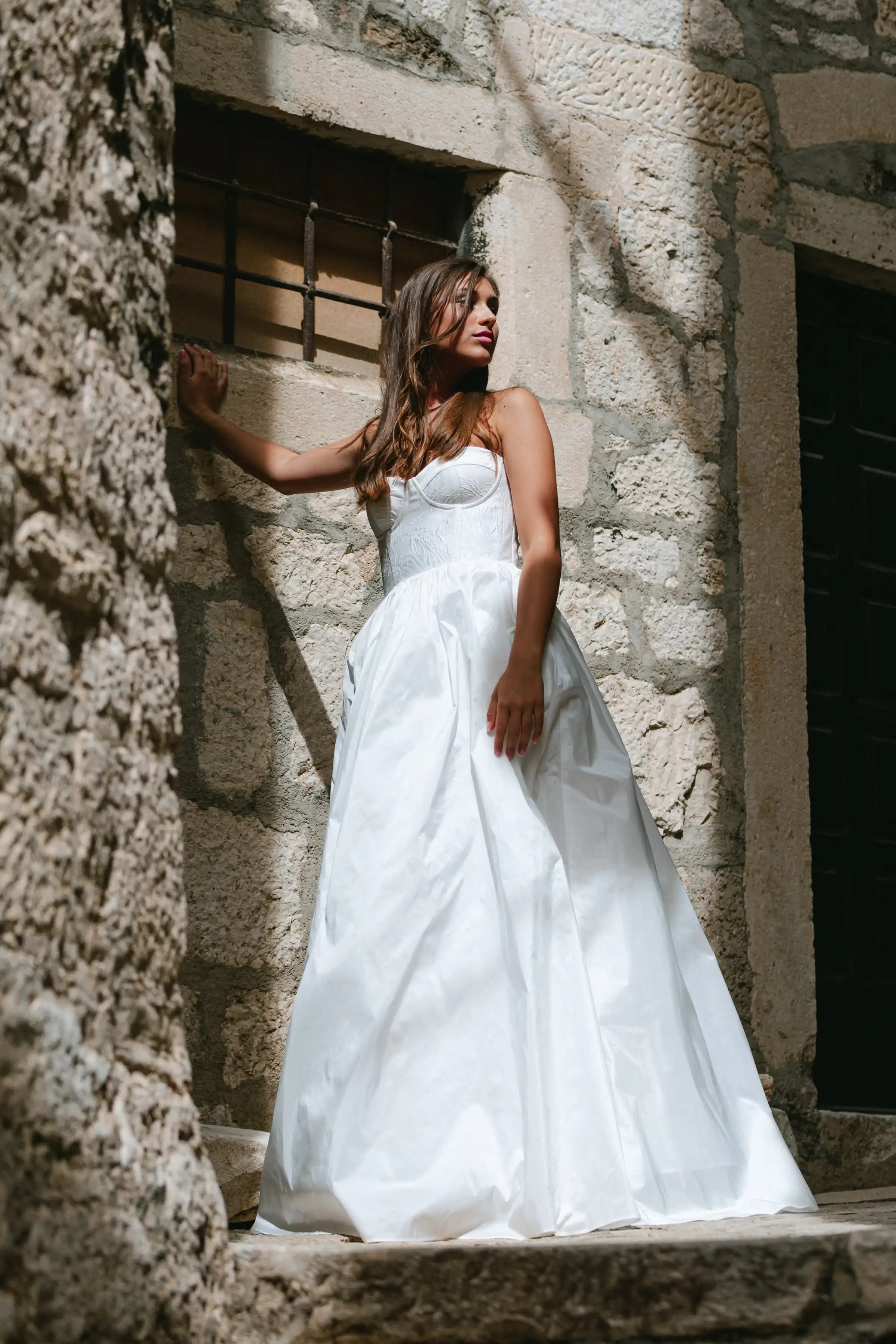Bride in a strapless gown beside a stone archway.