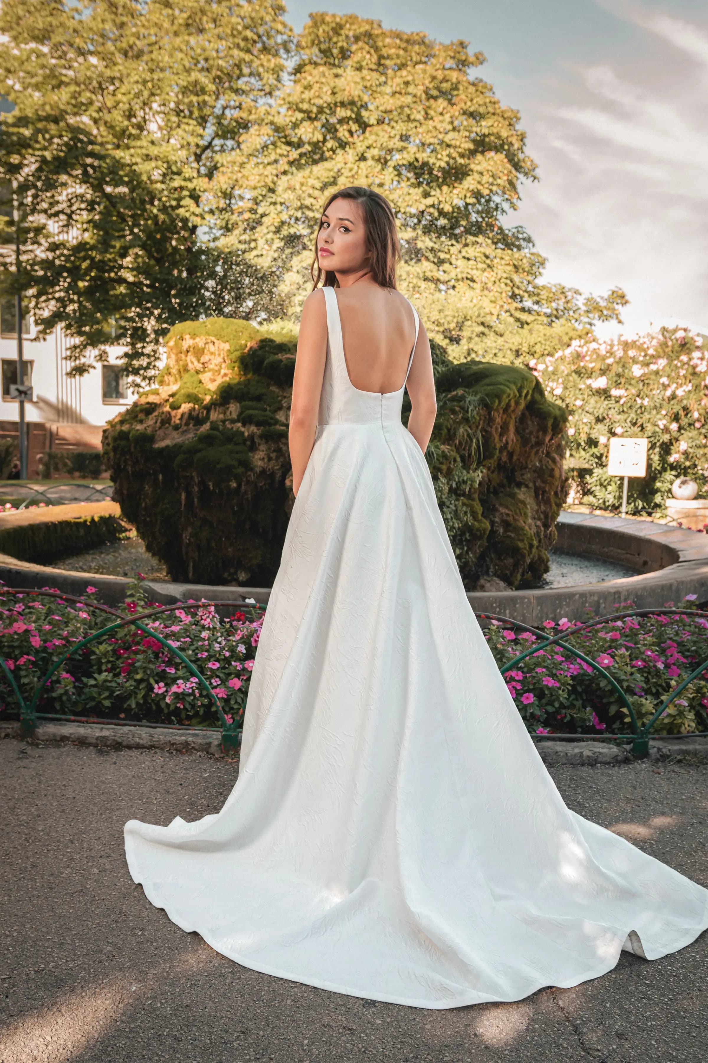Bride showing the open back of a gown in a formal garden.