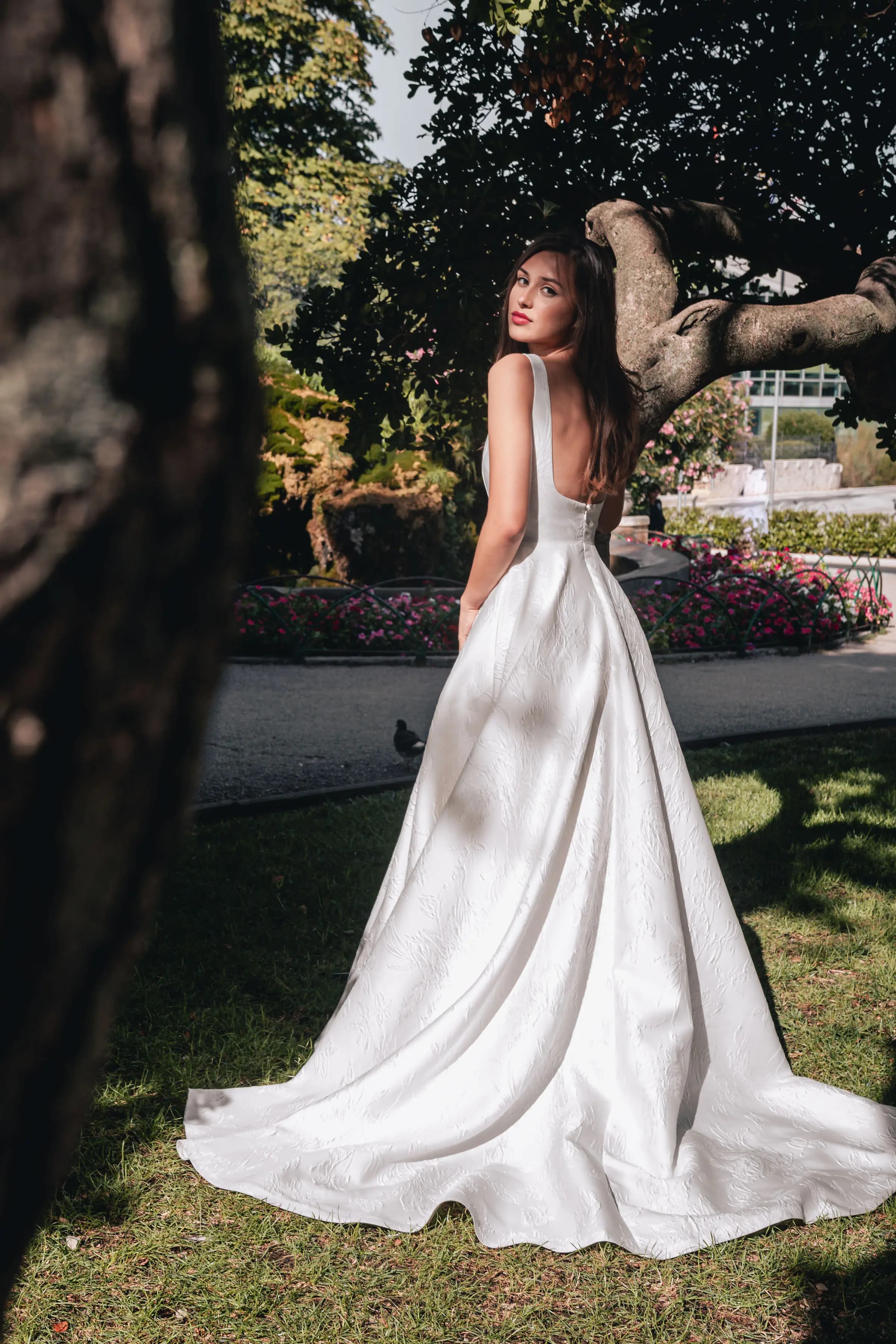 Bride showing the back of a gown beside a garden sculpture.